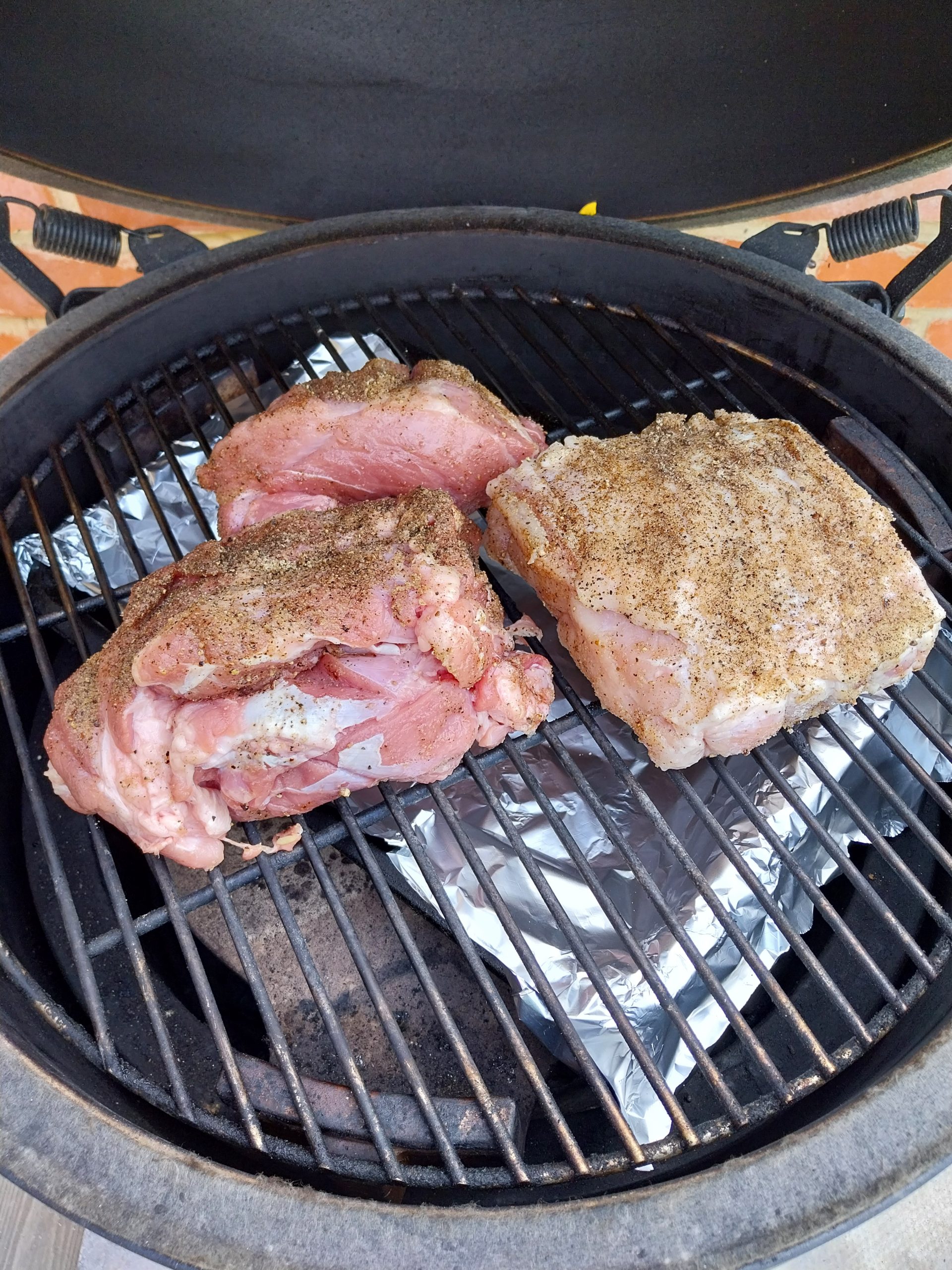 Two pieces of seasoned UK supermarket pork shoulder going on the BGE Large grate at the start of a 110°C low-and-slow cook — the natural two-piece state once the skin and fat layer were peeled back.