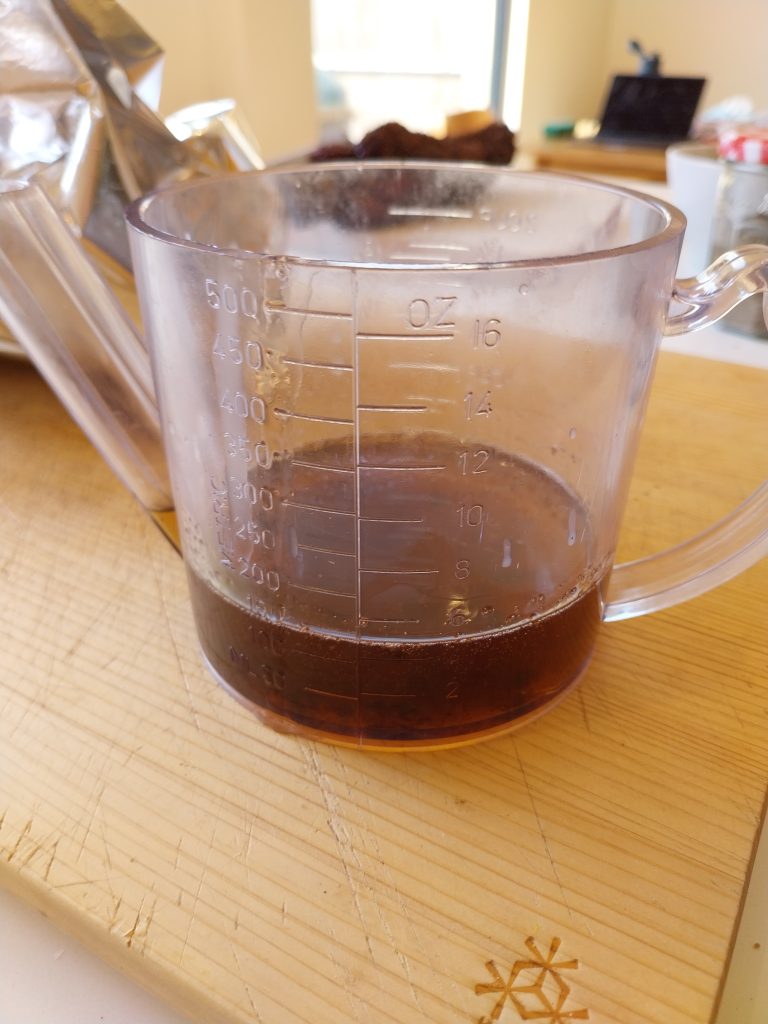 Rendered beef short rib tallow in a glass measuring jug, dark amber from four hours of slow oak-smoke render in the drip tray under the BGE Large ConvEGGtor.