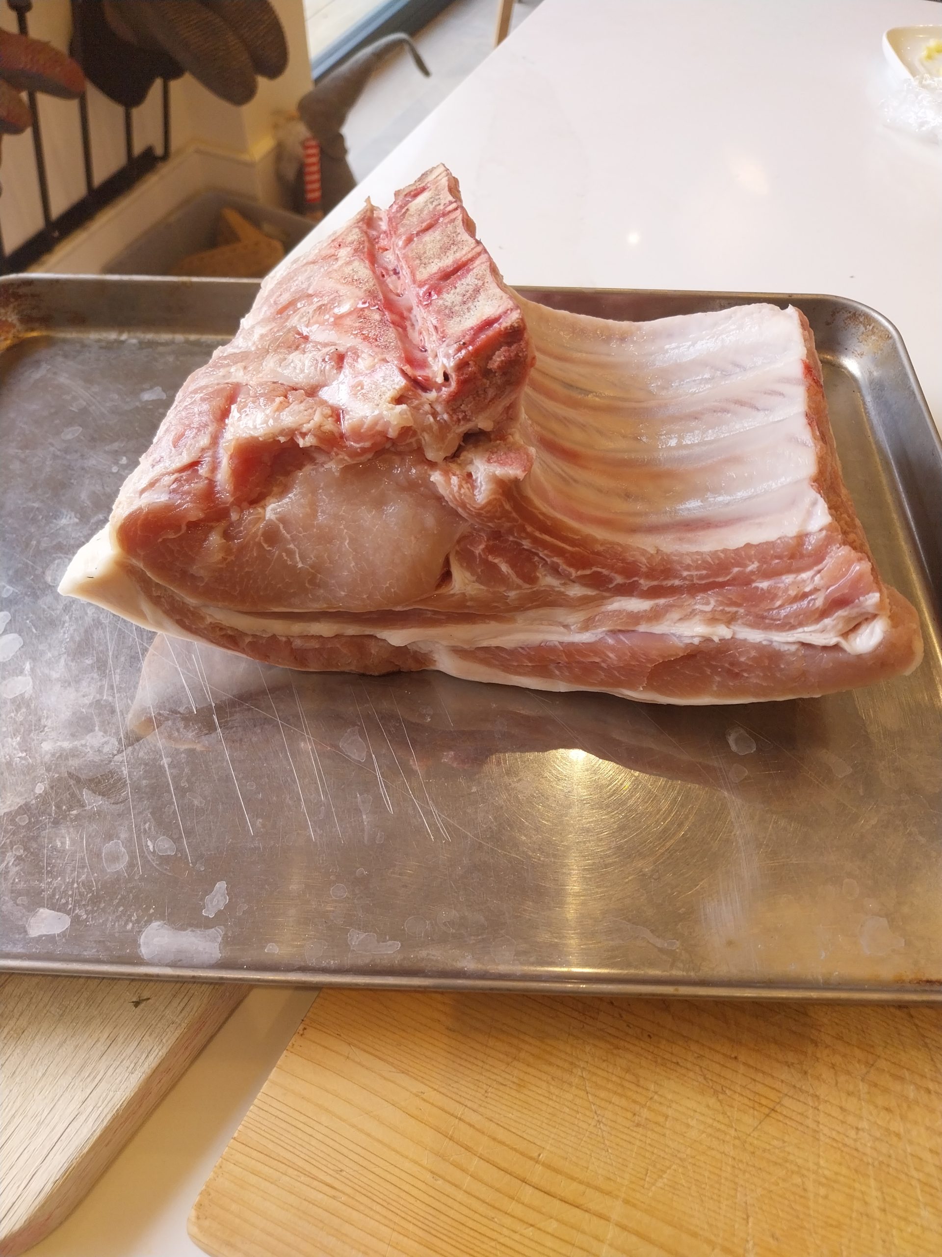 Bone-in pork loin rack with 2:1:0.5 SPG rub pressed into the surface, fat side up, chined rib bones visible underneath — ready for the kamado