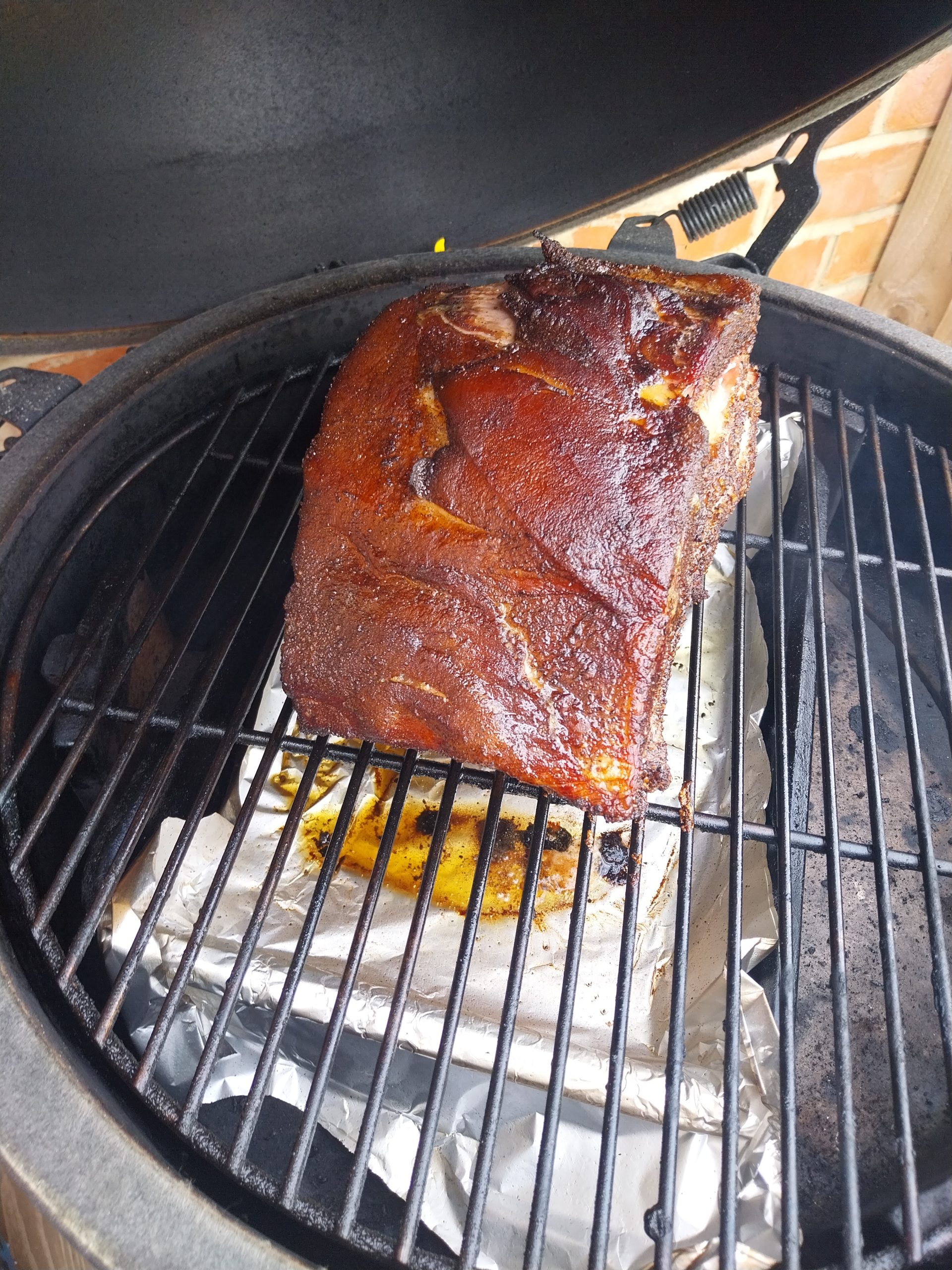 Bone-in pork loin foil-resting on a wooden carving rack just out of the cold oven after 40 minutes — bark set on the fat cap, bones still attached at the base