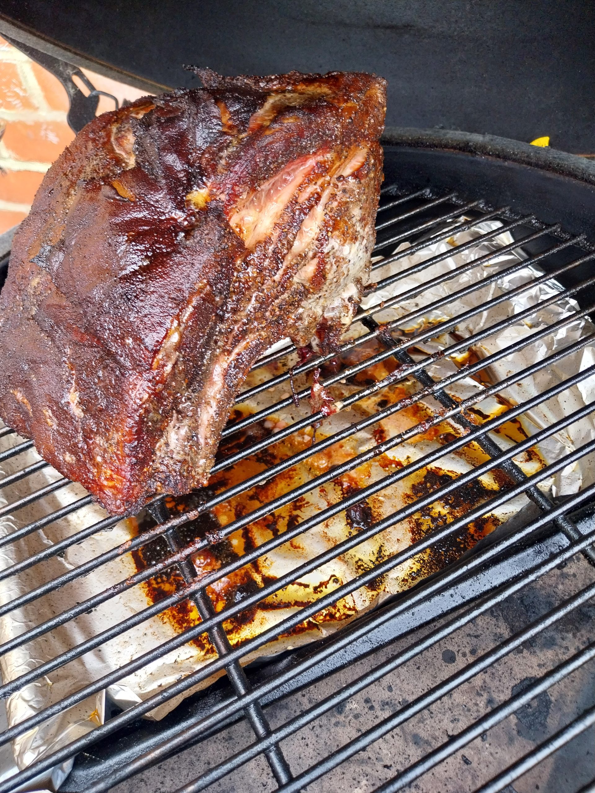 Whole bone-in pork loin rack just off the BGE Large grid post-cook, fat-cap bark on top, rib bones along the base — the cooked rack before it goes to rest