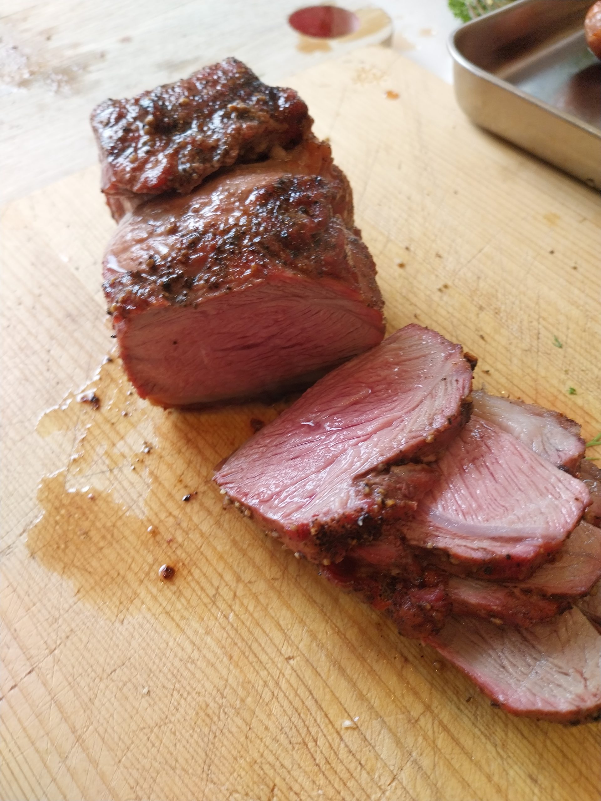 Sliced lamb rump on a wooden carving board, bright cherry-pink medium-rare interior, dark peppery crust, second piece sitting behind — 31 May 2026 cook on the BGE Large