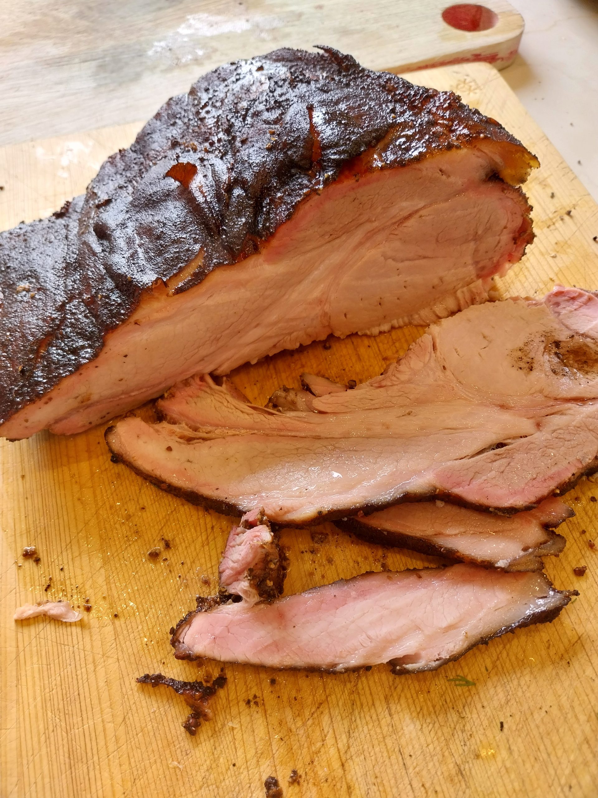 Sliced bone-in pork loin on a wooden board, even medium-pink colour throughout with a visible smoke ring along the outer edge — cooked on the BGE Large at 140°C indirect over oak