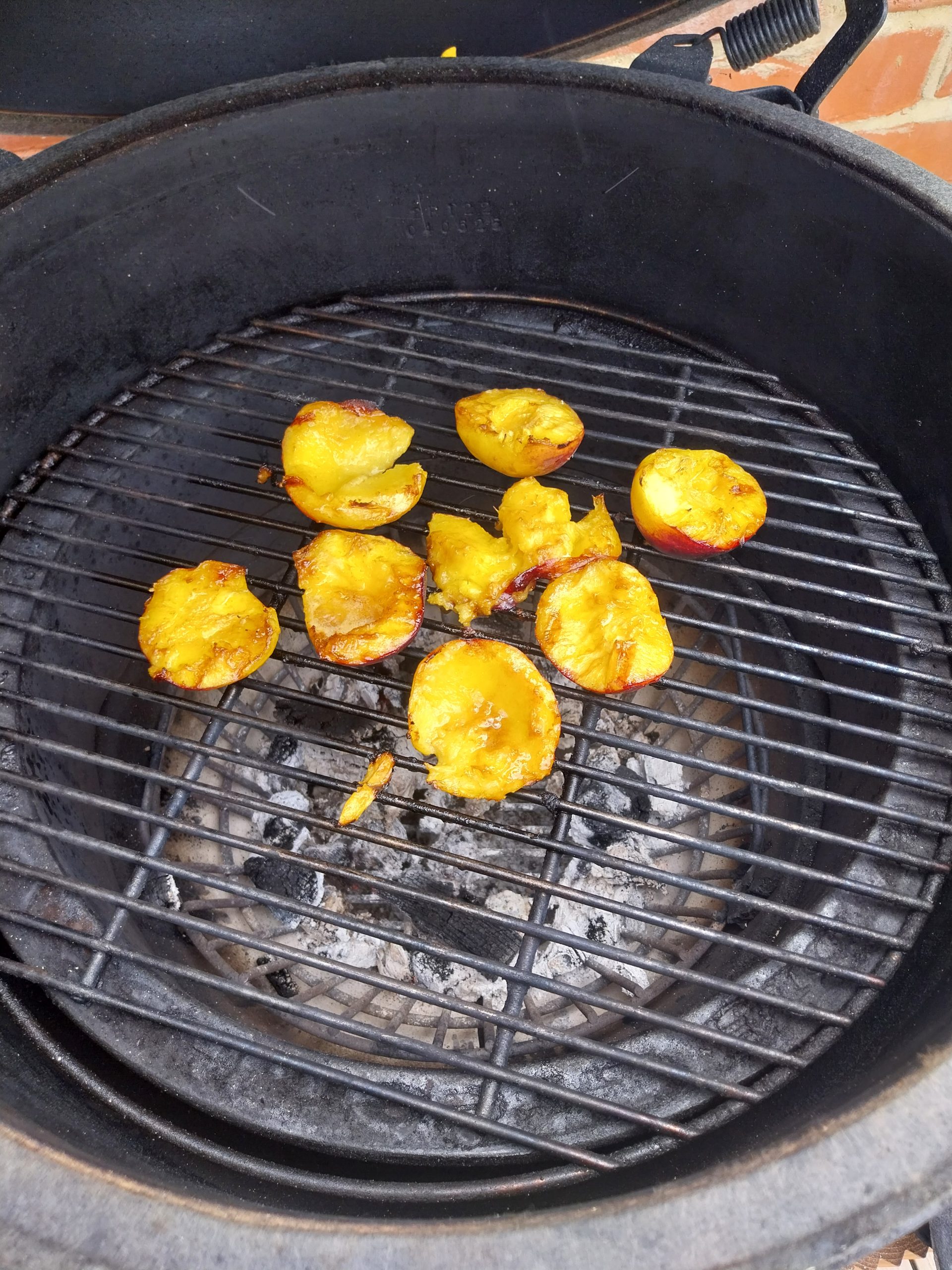 Four peaches halved and caramelised, cut-side up on the Big Green Egg Large's grid over a bed of spent white ash — direct heat, deflector out, 31 May 2026