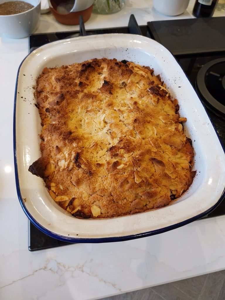 Finished apple and summer berry crumble in a white enamel dish with a blue rim, top golden brown with flaked almonds through it
