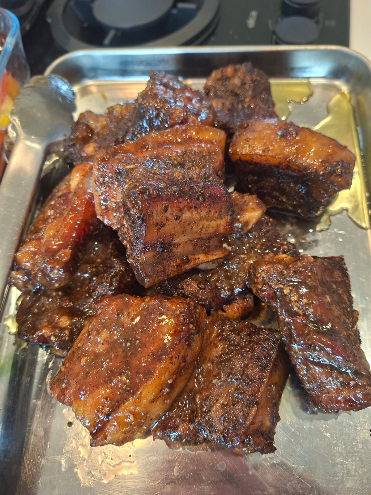 A pile of finished burnt-end cubes on a metal serving tray — dark-glazed and glossy, chutney reduction pooling at the base, ready to plate for the adults' table.
