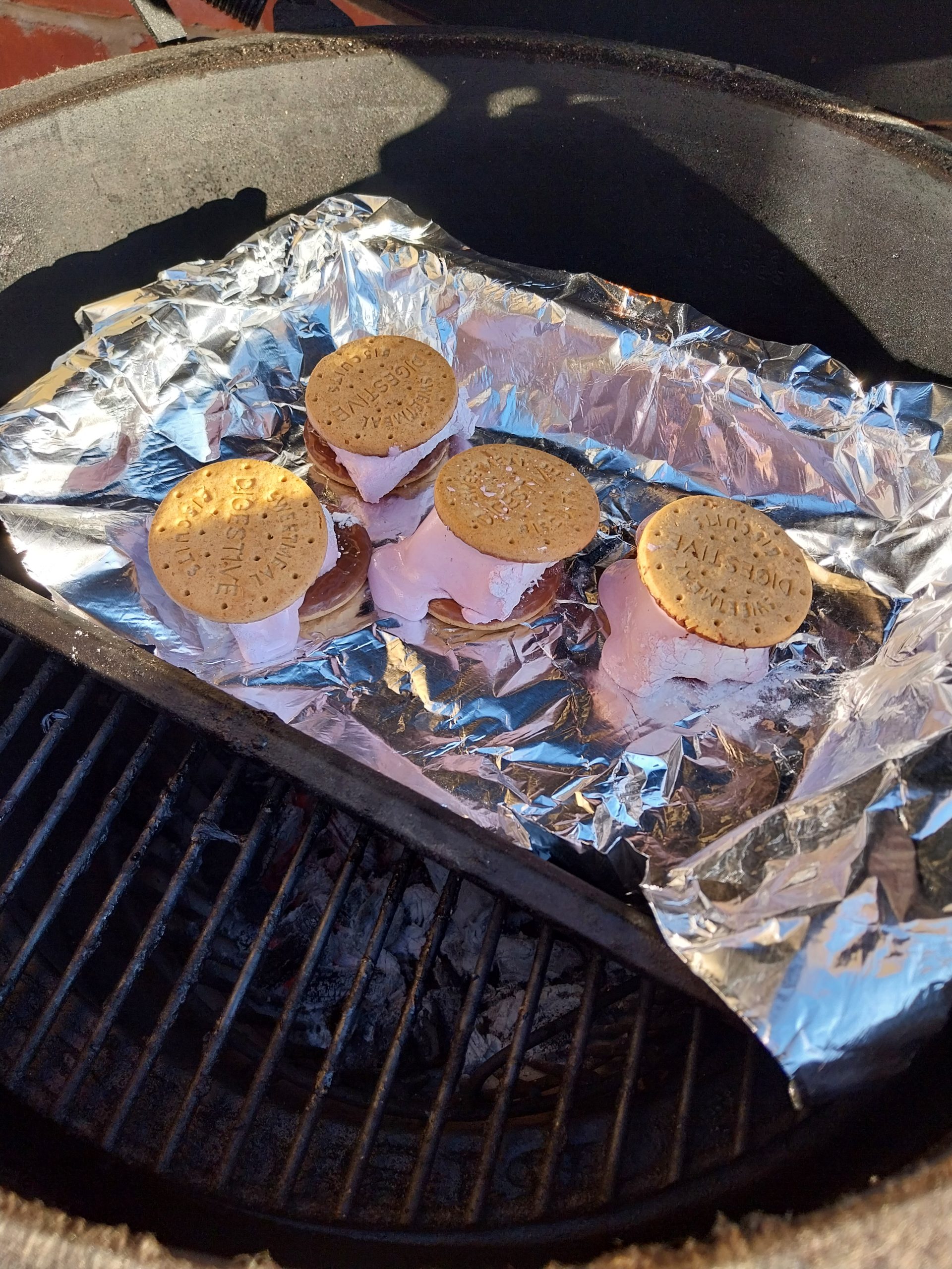 The same four s'mores two and a half minutes later, the marshmallow spread flat out from between the biscuits across the foil