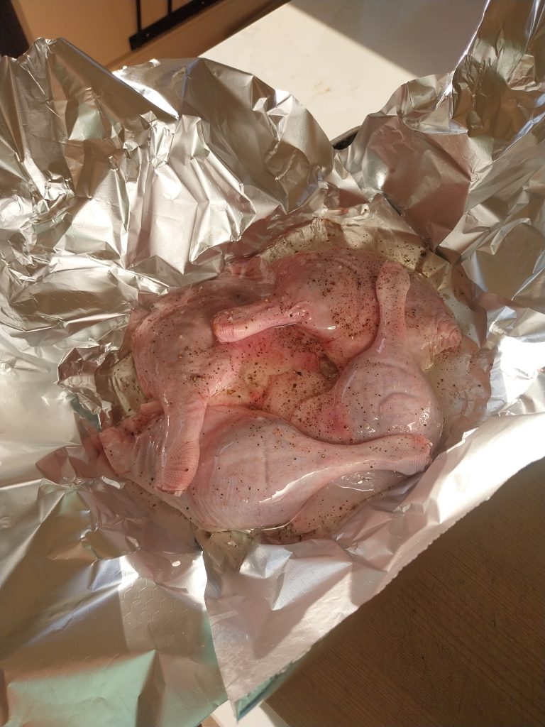 Four duck legs seasoned with salt and pepper, sitting in sunflower oil in a foil tray before they go on the kamado