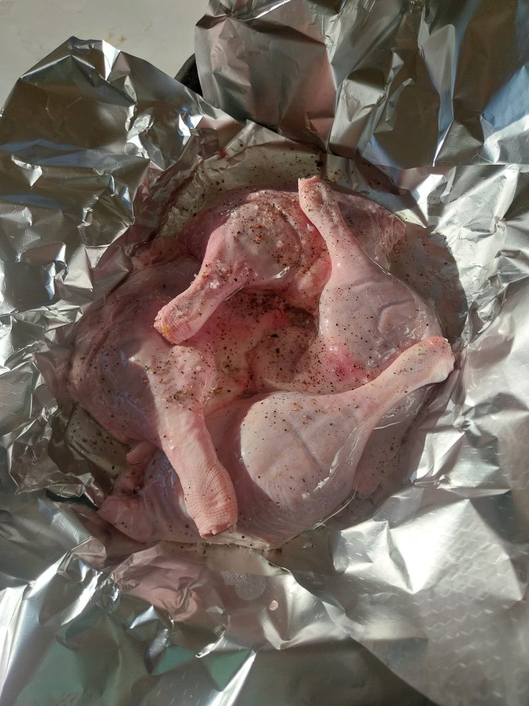 Four duck legs seasoned in oil in a foil boat, seen from above, before they went on.