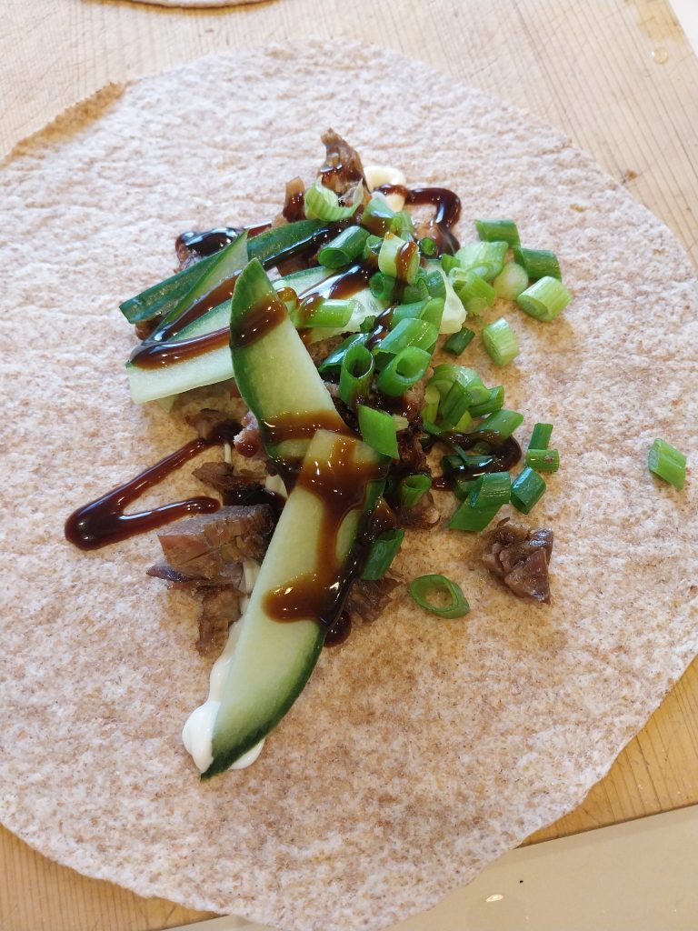 A finished duck wrap — chopped duck, hoisin, cucumber batons and chopped spring onions on a flour tortilla