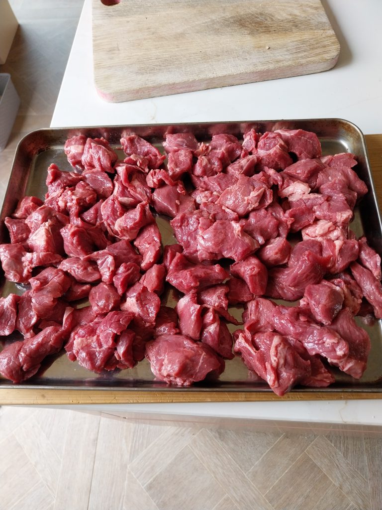 Two kilos of raw diced beef chuck spread on a metal tray, cut to a small stewing dice