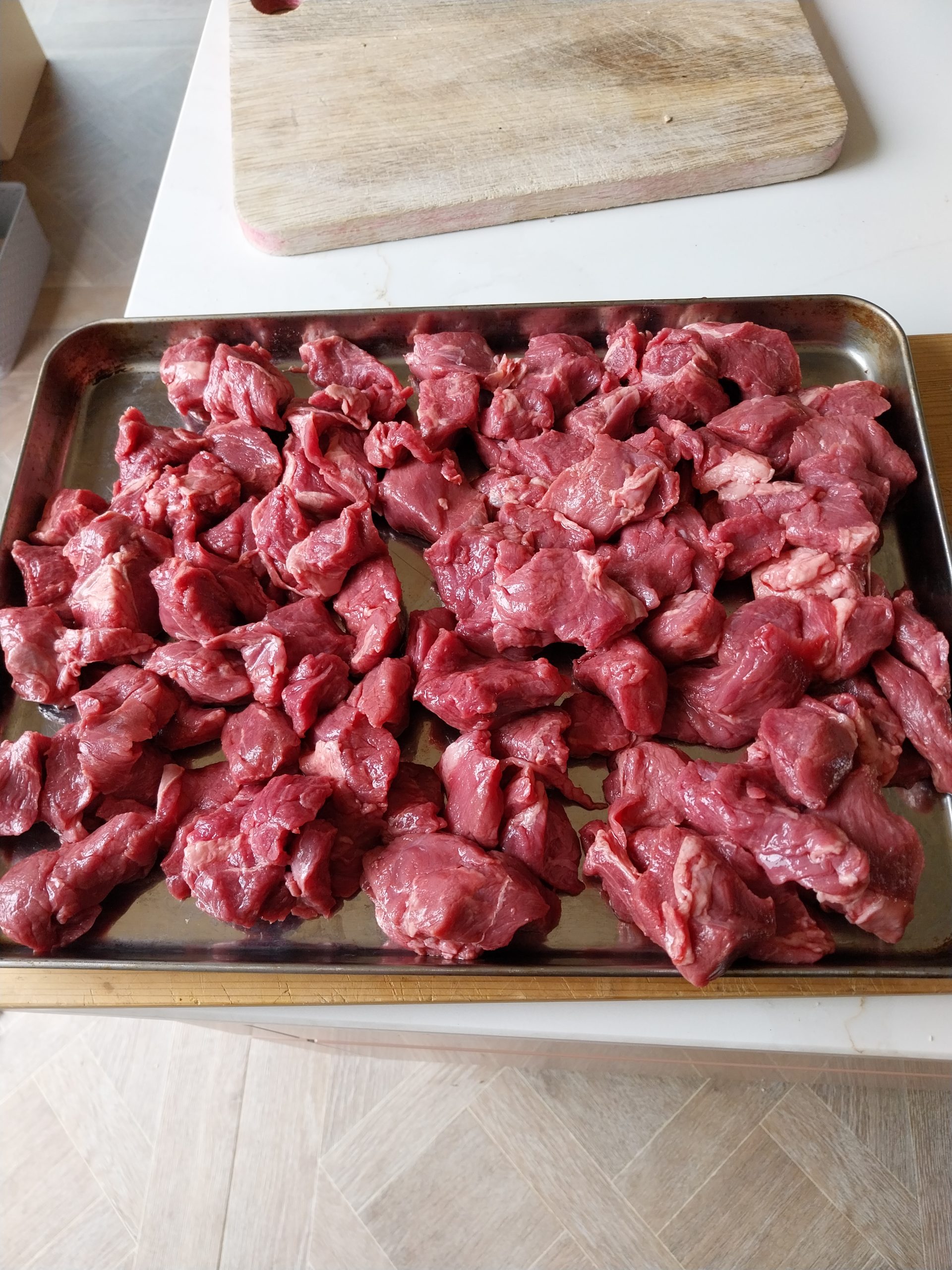 Two kilos of raw diced beef chuck spread on a metal tray, cut to a small stewing dice