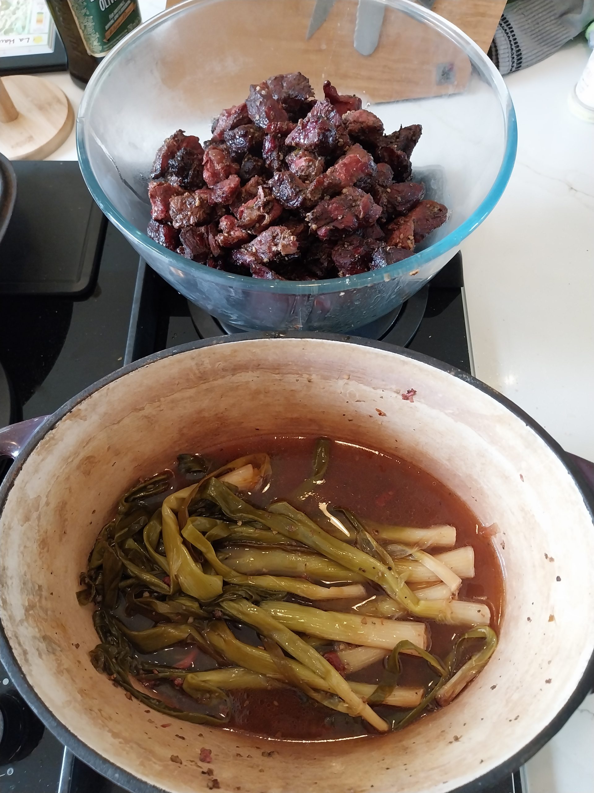 A glass bowl of braised beef chuck above the cast-iron pot, spring onions still whole in the reduced ale liquor
