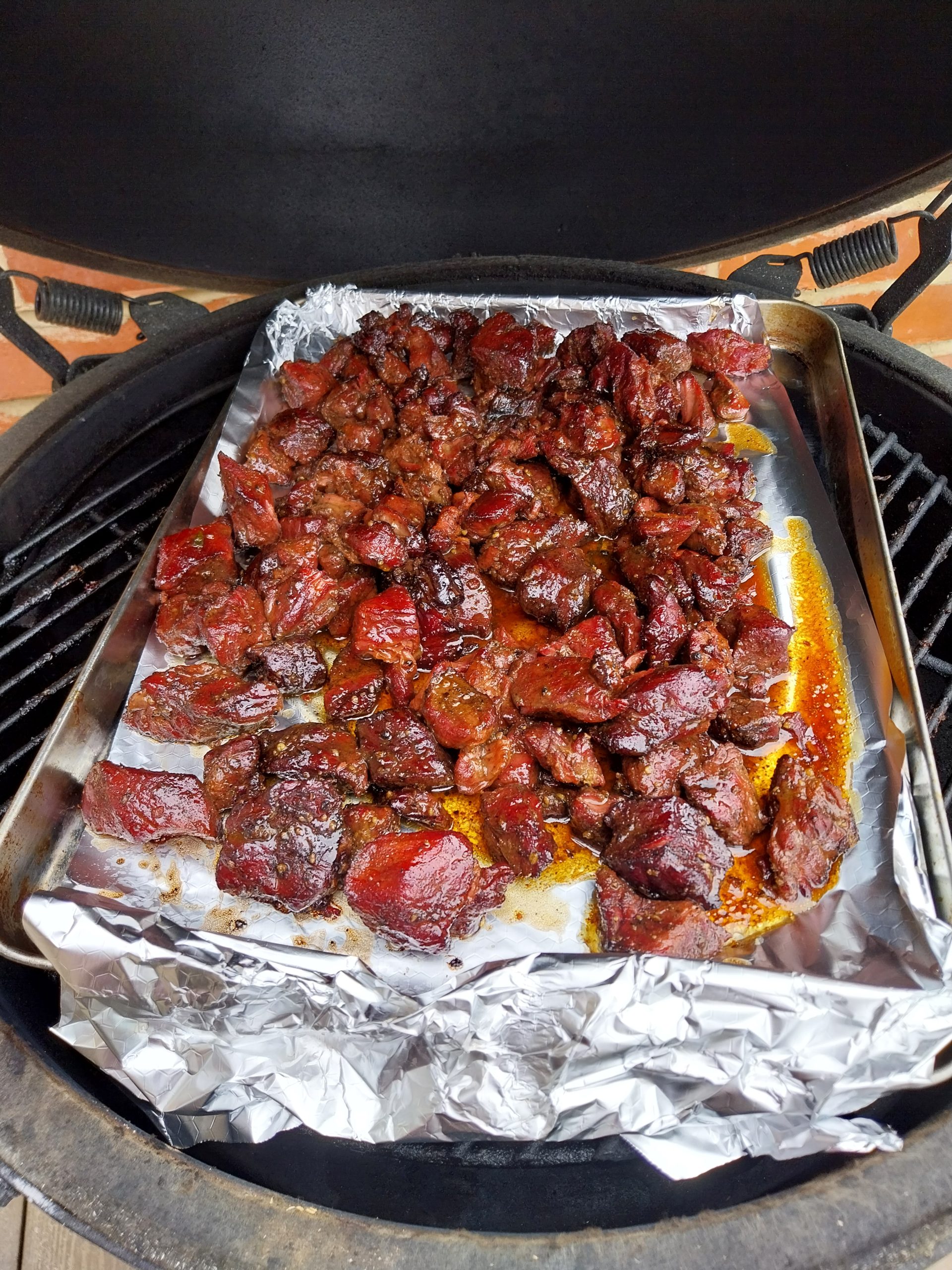 A foil-lined tray of glazed beef chuck cubes going back onto the kamado grate for the final twenty-eight minutes, dome open