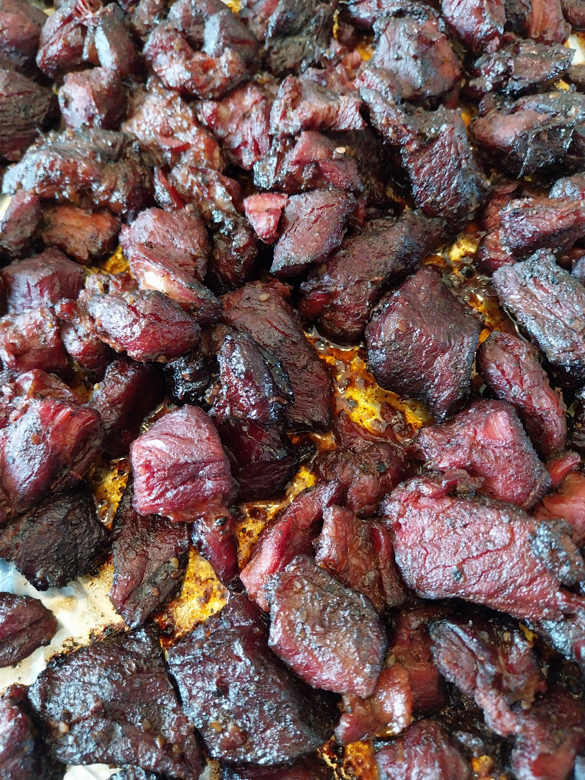 Poor man's burnt ends of beef chuck coming off the kamado, dark and glossy with glaze, in a foil-lined tray