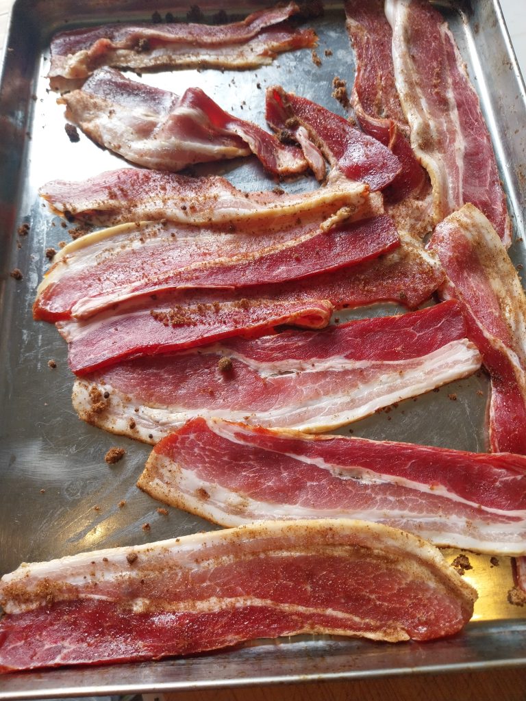 Smoked streaky rashers on a metal tray with dark brown sugar rubbed in, ready for candied bacon