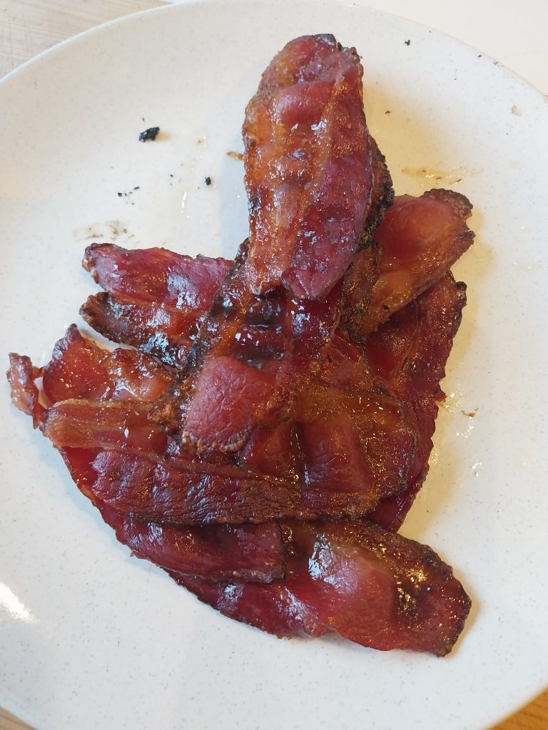 Candied bacon piled on a white plate after coming off the kamado