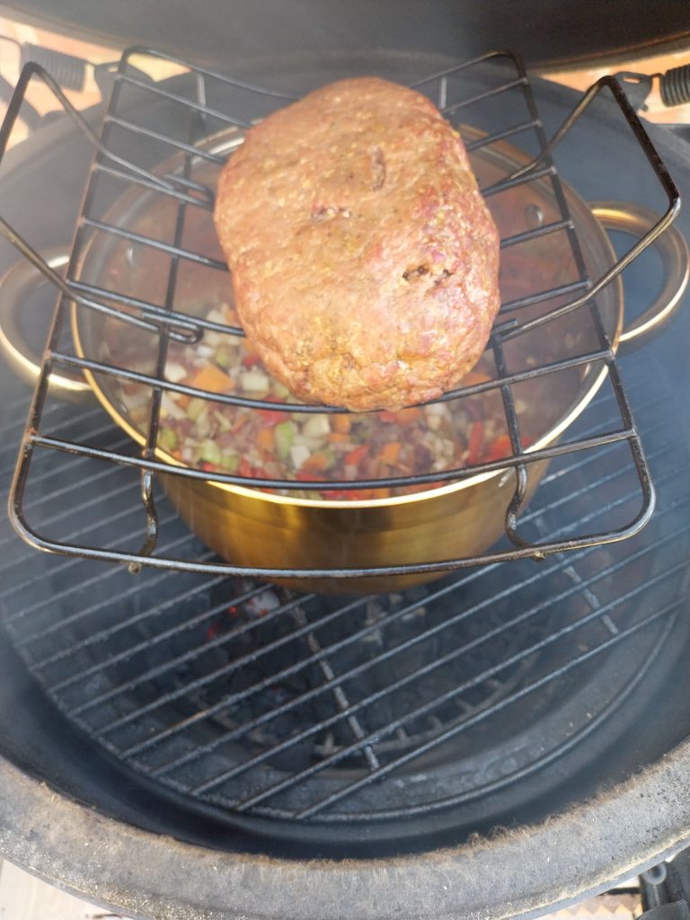 The beef mince shaped into a ball on a rack above the chilli pot on the Egg, starting to smoke.