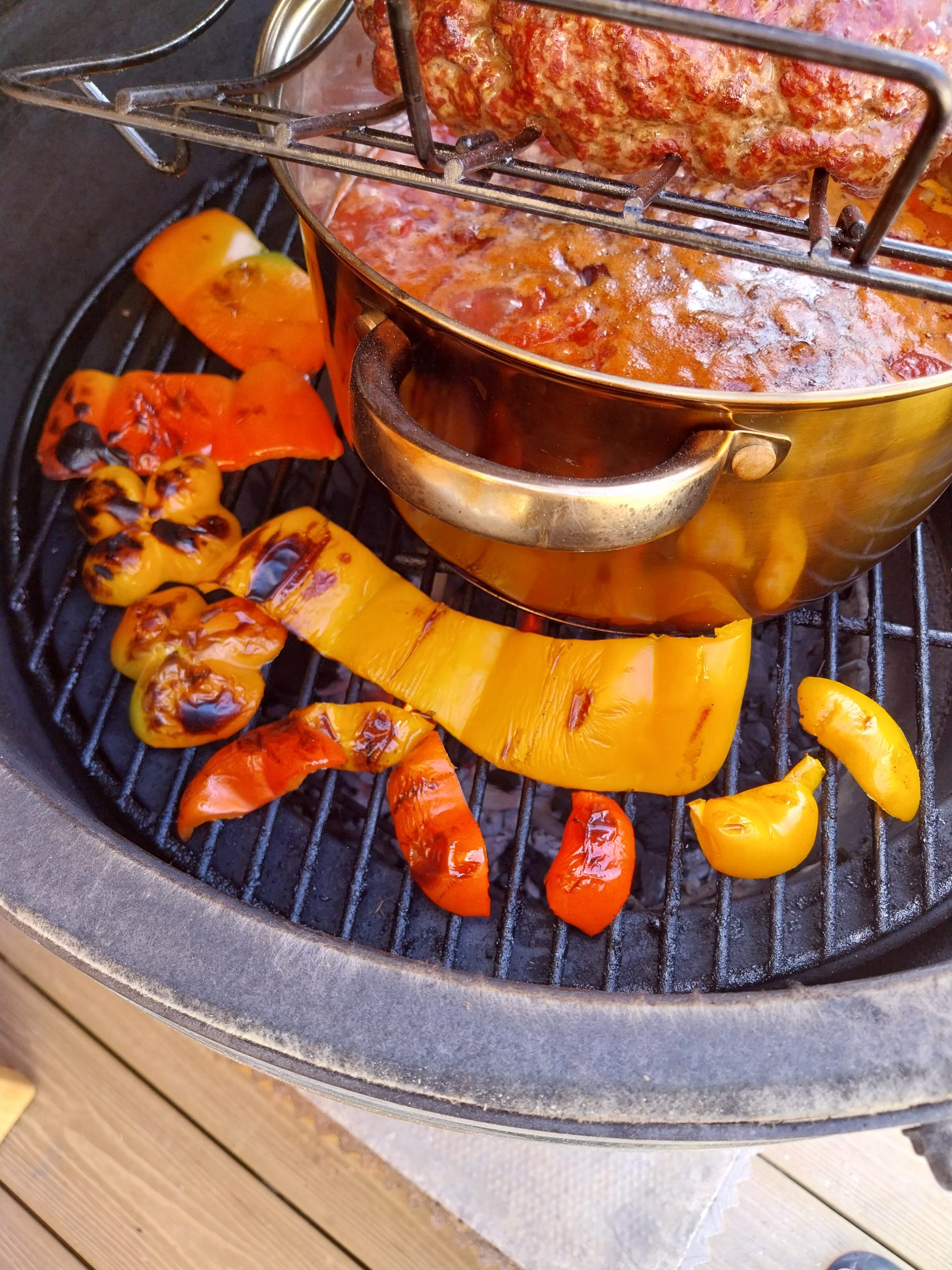 Sliced peppers charring on the grid over live coals, blistered and blackened in places, with the chilli pot alongside on the same fire