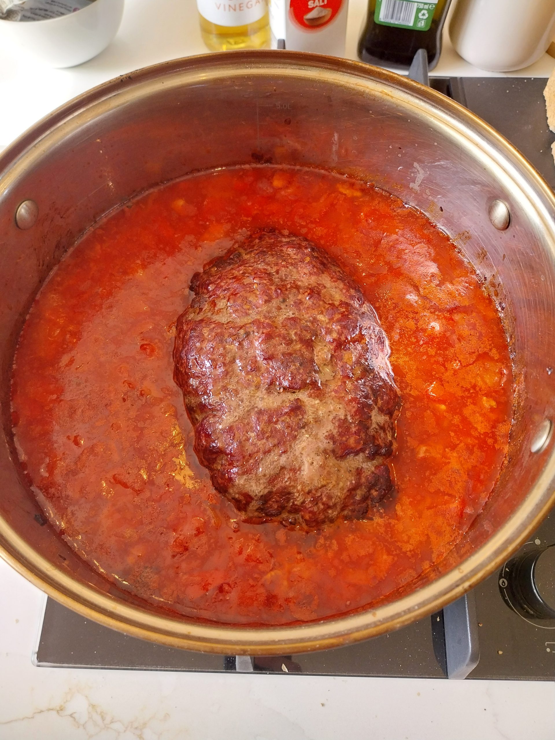 The whole cooked mince ball sitting in the tomato sauce in the pot, before it was broken up with a wooden spoon.