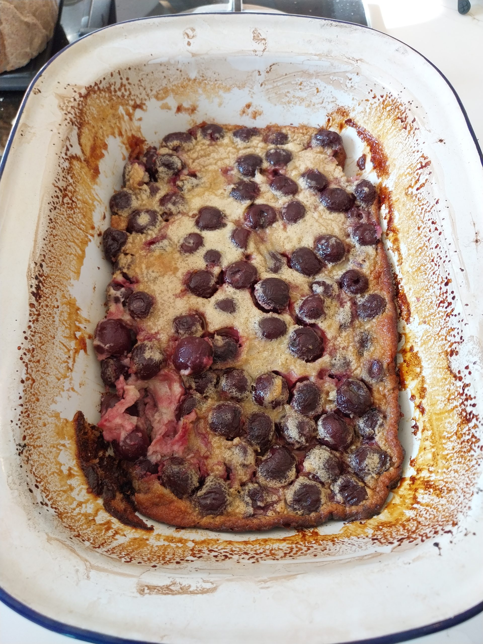 The finished clafoutis in its enamelled steel dish, sunk flat across the middle after coming off the fire