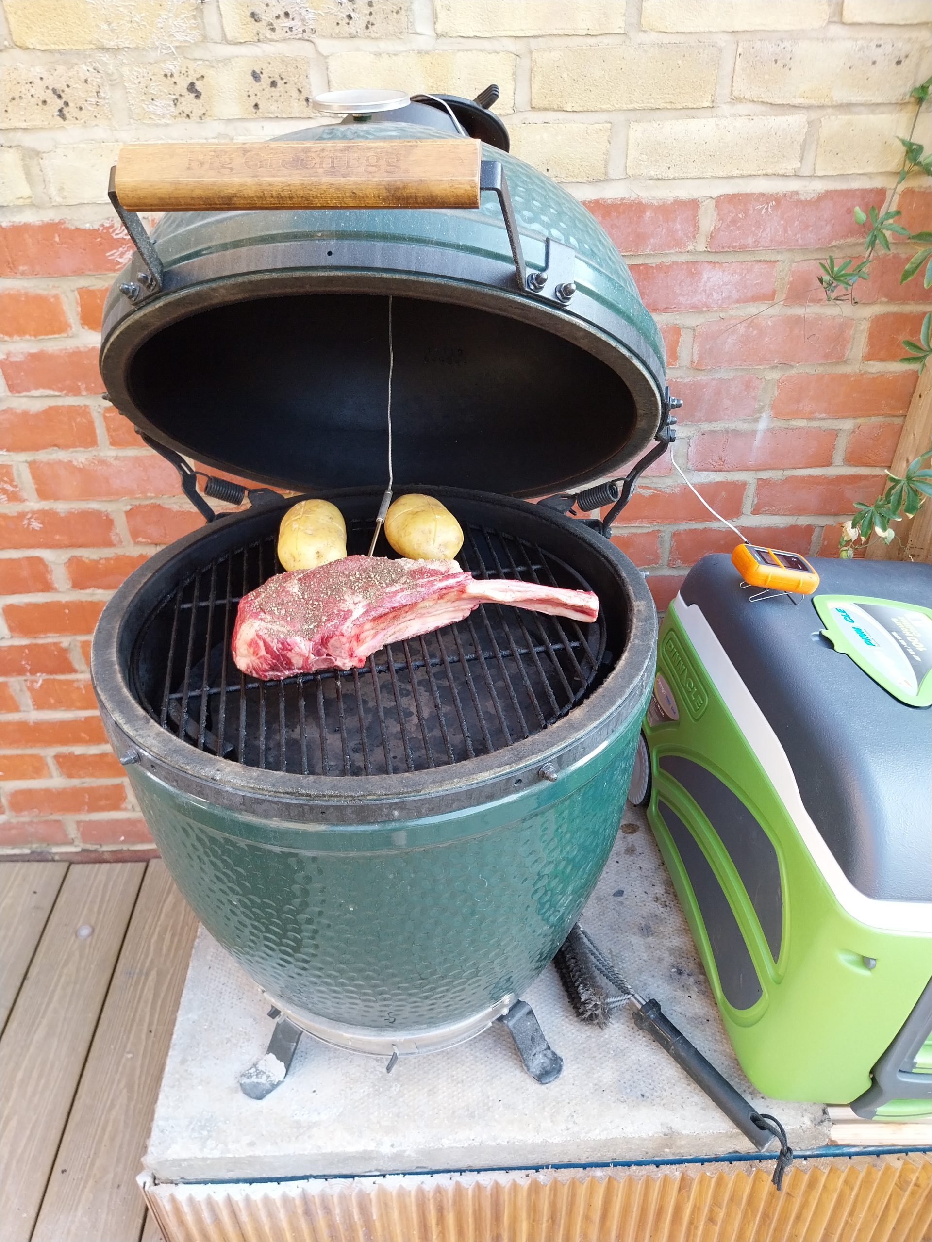 The tomahawk on the Big Green Egg Large grid with two baking potatoes, the leave-in probe in the thickest part of the steak