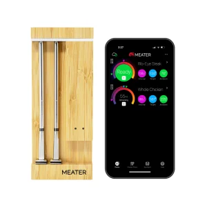 MEATER Pro Duo — two stainless probes in the bamboo charging block, beside a phone running the MEATER app with two cooks on screen. Image: MEATER UK.