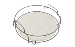 Big Green Egg Dual Zone Deflector Kit — a cream ceramic disc split into two half-moons, seated in a stainless steel wire cradle with looped handles, Big Green Egg lettering embossed on the face