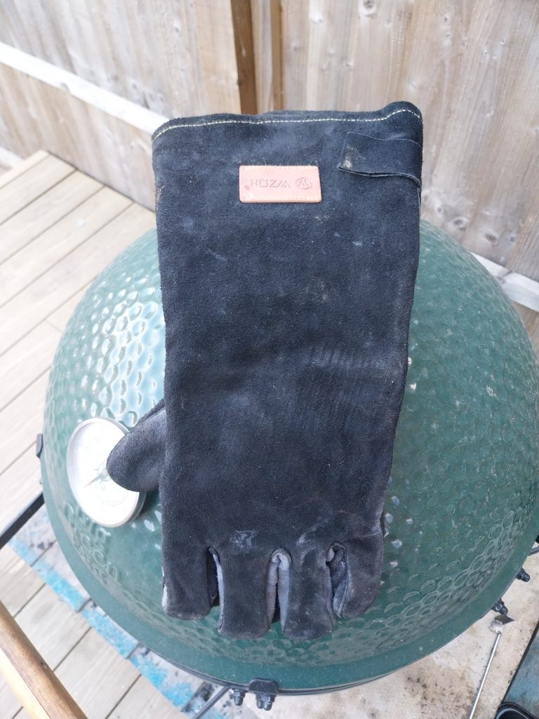 A long-cuffed leather BBQ glove standing upright on the Big Green Egg Large's closed lid
