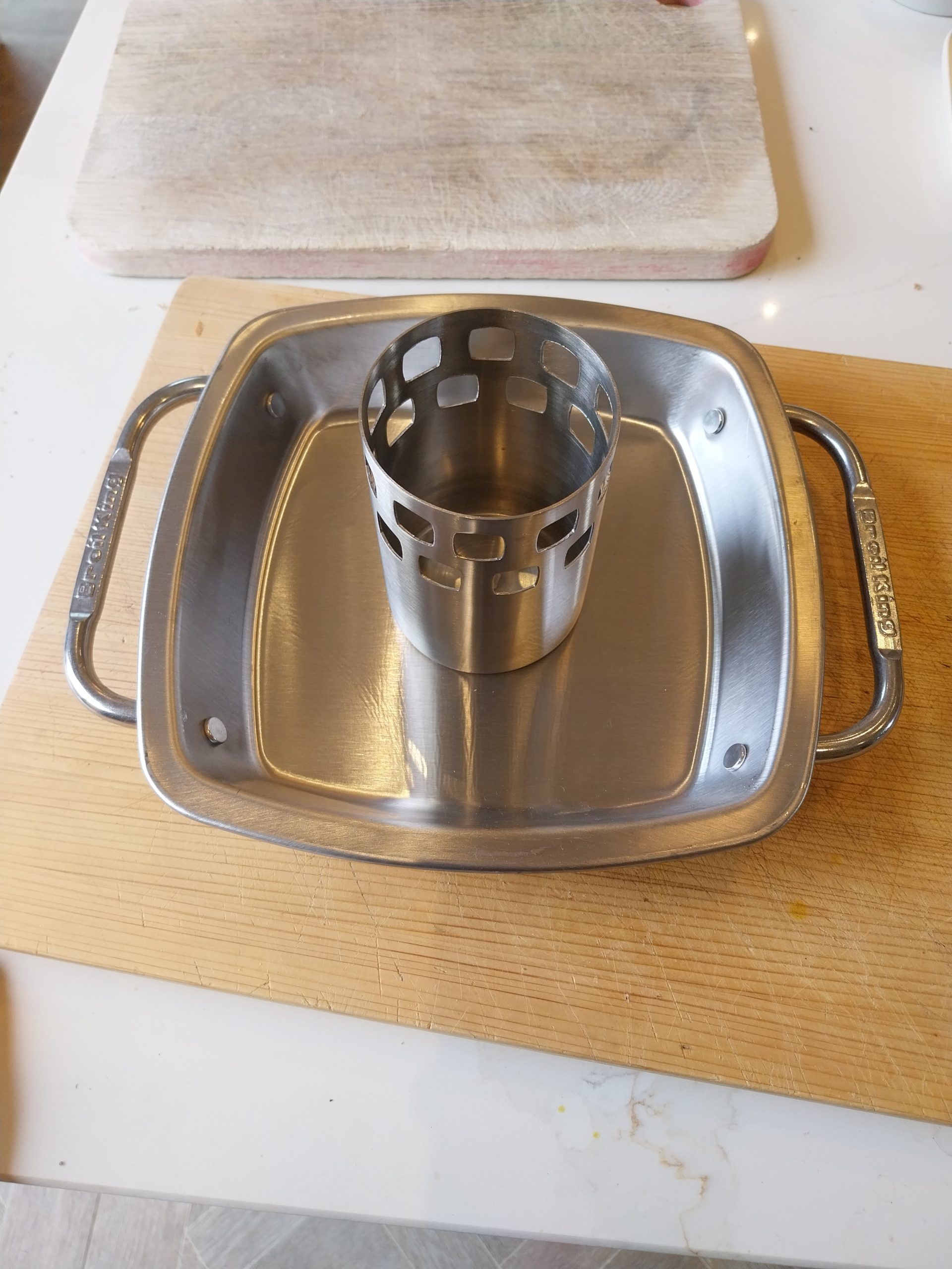 A stainless steel Broil King vertical roaster, new and unused, standing in its drip tray on a wooden board