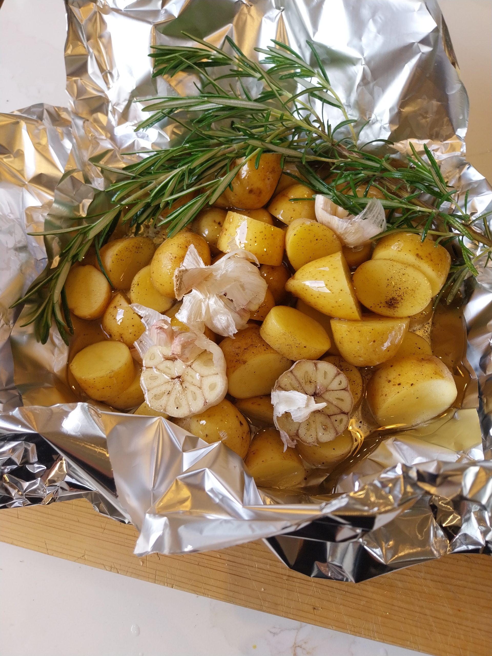 New potatoes, halved garlic heads and rosemary in a doubled sheet of foil with sunflower oil poured in, before the packet is crimped closed