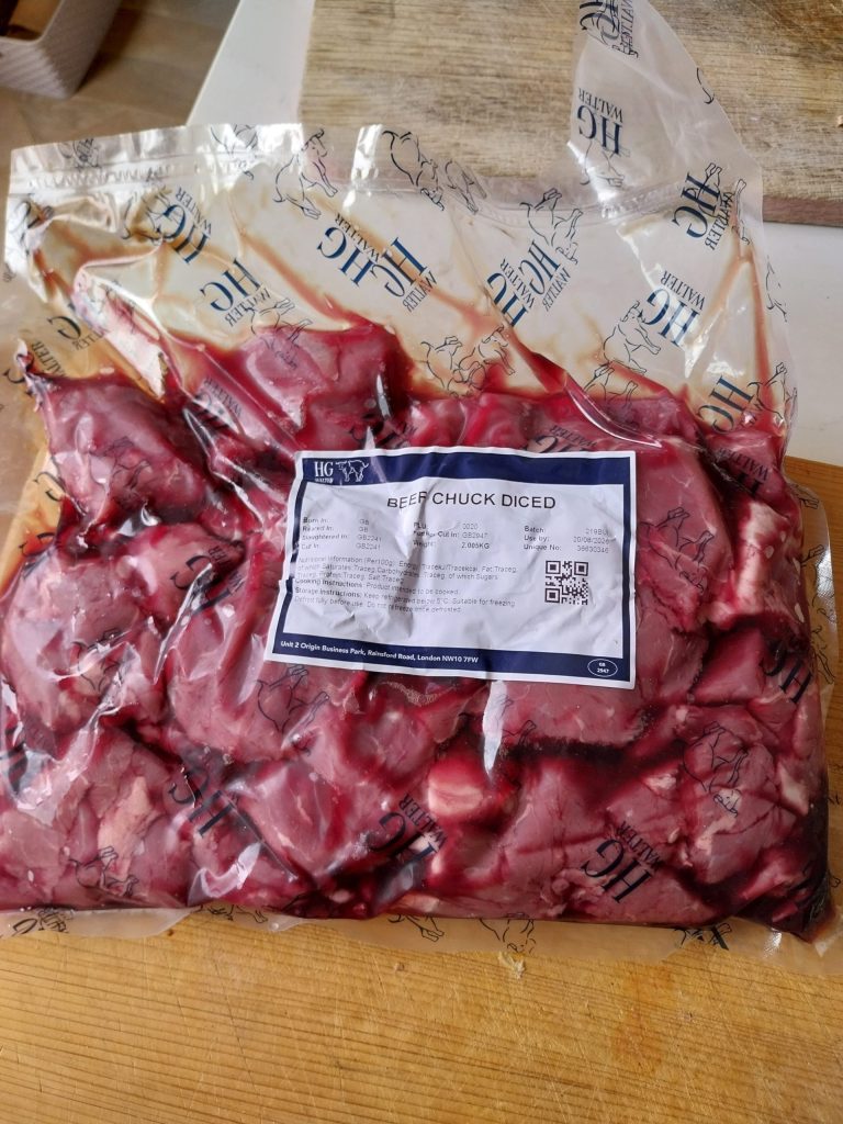 A vacuum-packed pack of diced beef chuck on a wooden worktop, the film printed with the HG Walter house mark and the label reading BEEF CHUCK DICED.