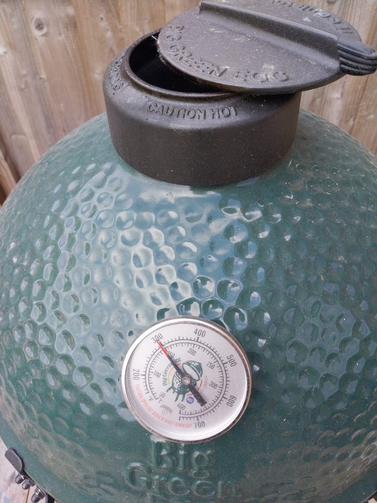 The cast-iron daisy wheel on the Big Green Egg Large's lid, partly closed, with the lid thermometer alongside
