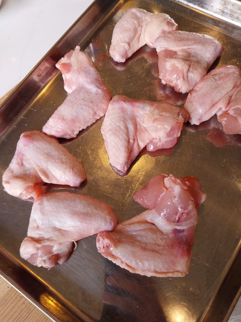 Raw chicken wings spread out on a steel tray on the worktop, salted and left uncovered to air-dry before the cook.