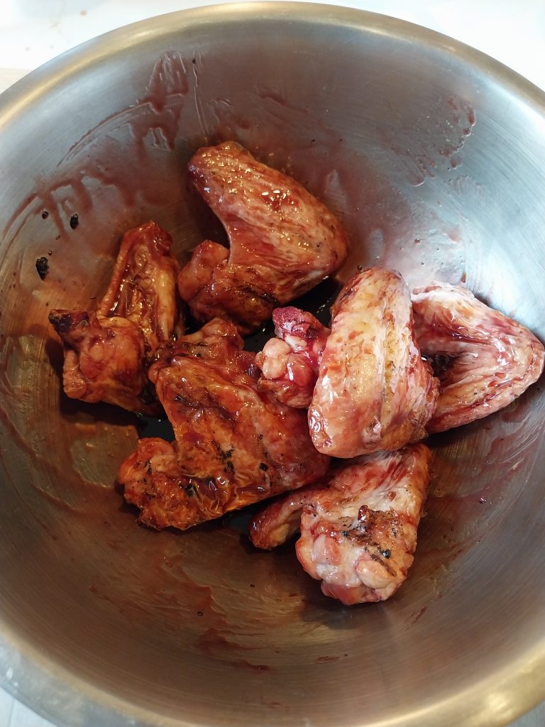 Chicken wings being tossed through the cherry glaze in a bowl, off the barbecue.
