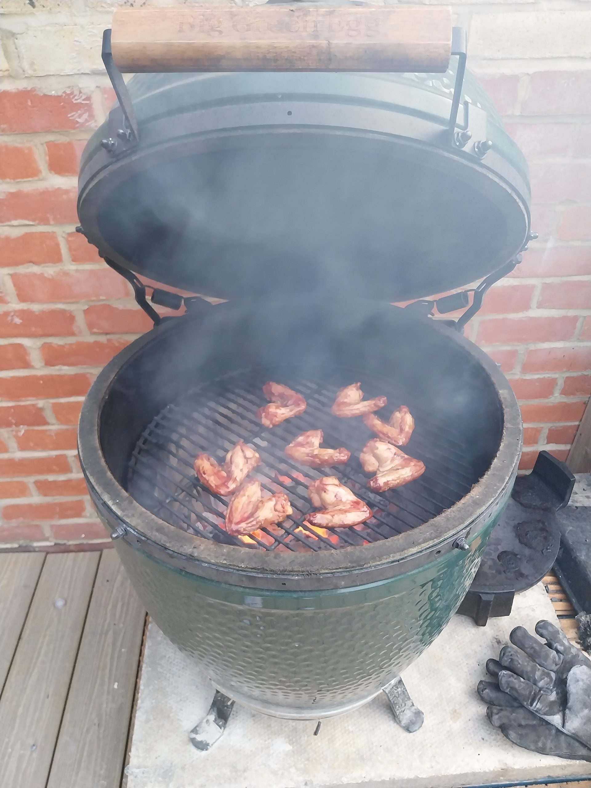 Chicken wings on the grate of a Big Green Egg with the lid up, live coals glowing directly underneath and smoke coming off.