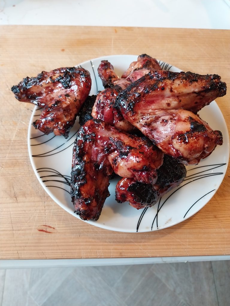The finished chicken wings piled on a white plate on a wooden board, glazed deep red-brown and blackened in patches at the edges.