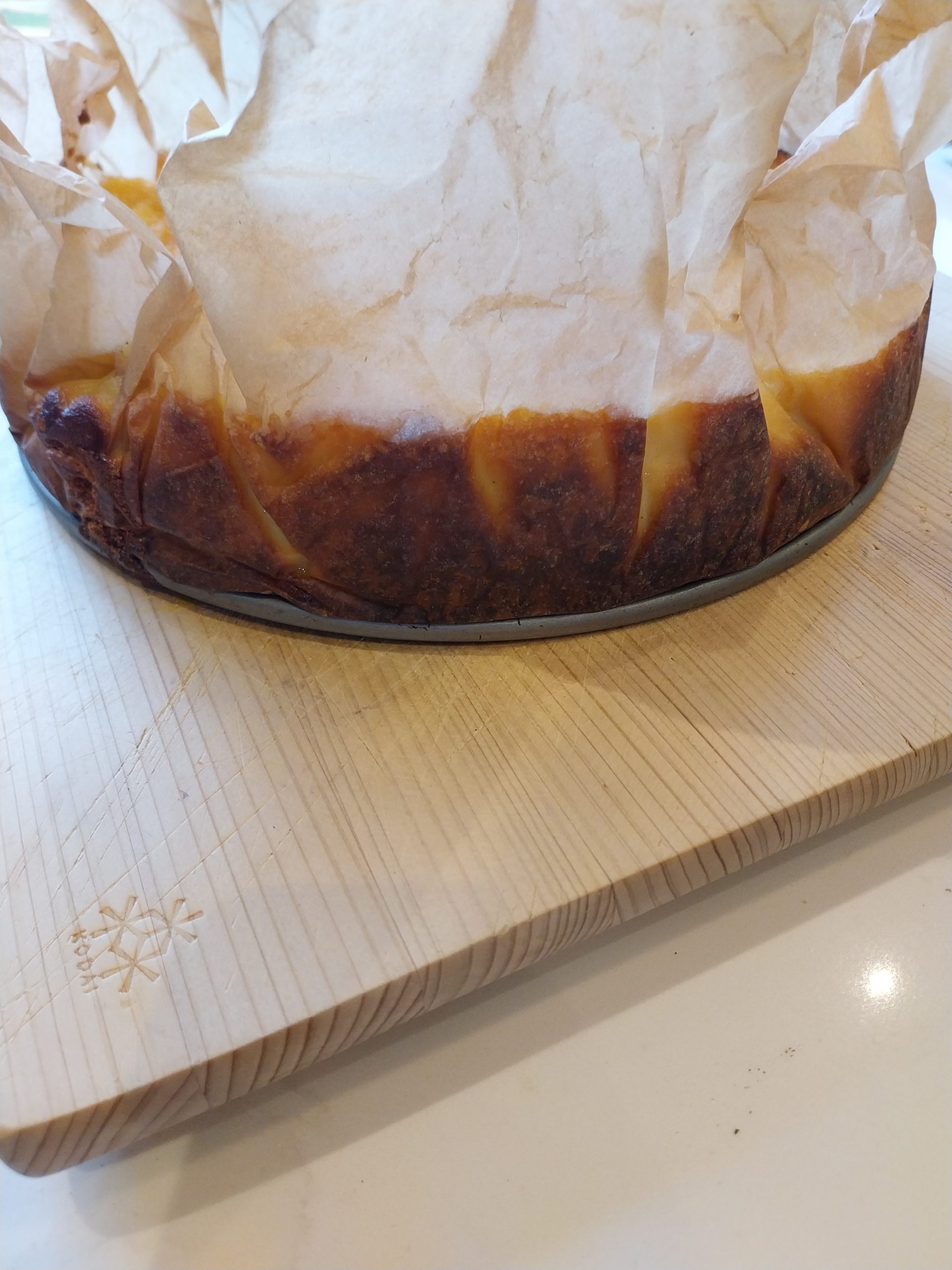 The side of the cheesecake on a wooden board, dark and burnt below the parchment