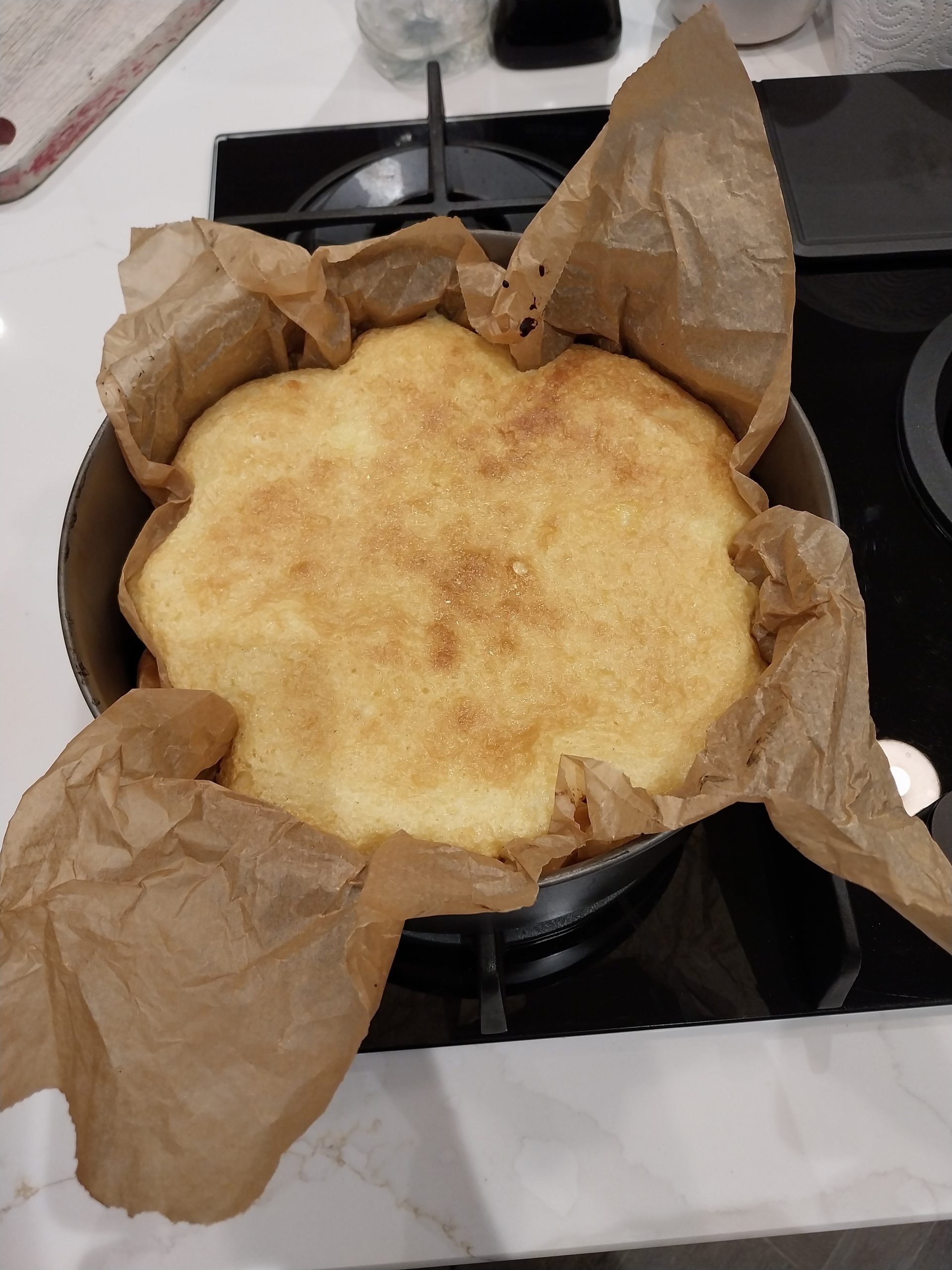 The baked cheesecake still in its parchment-lined tin, golden on top, cooling on the hob
