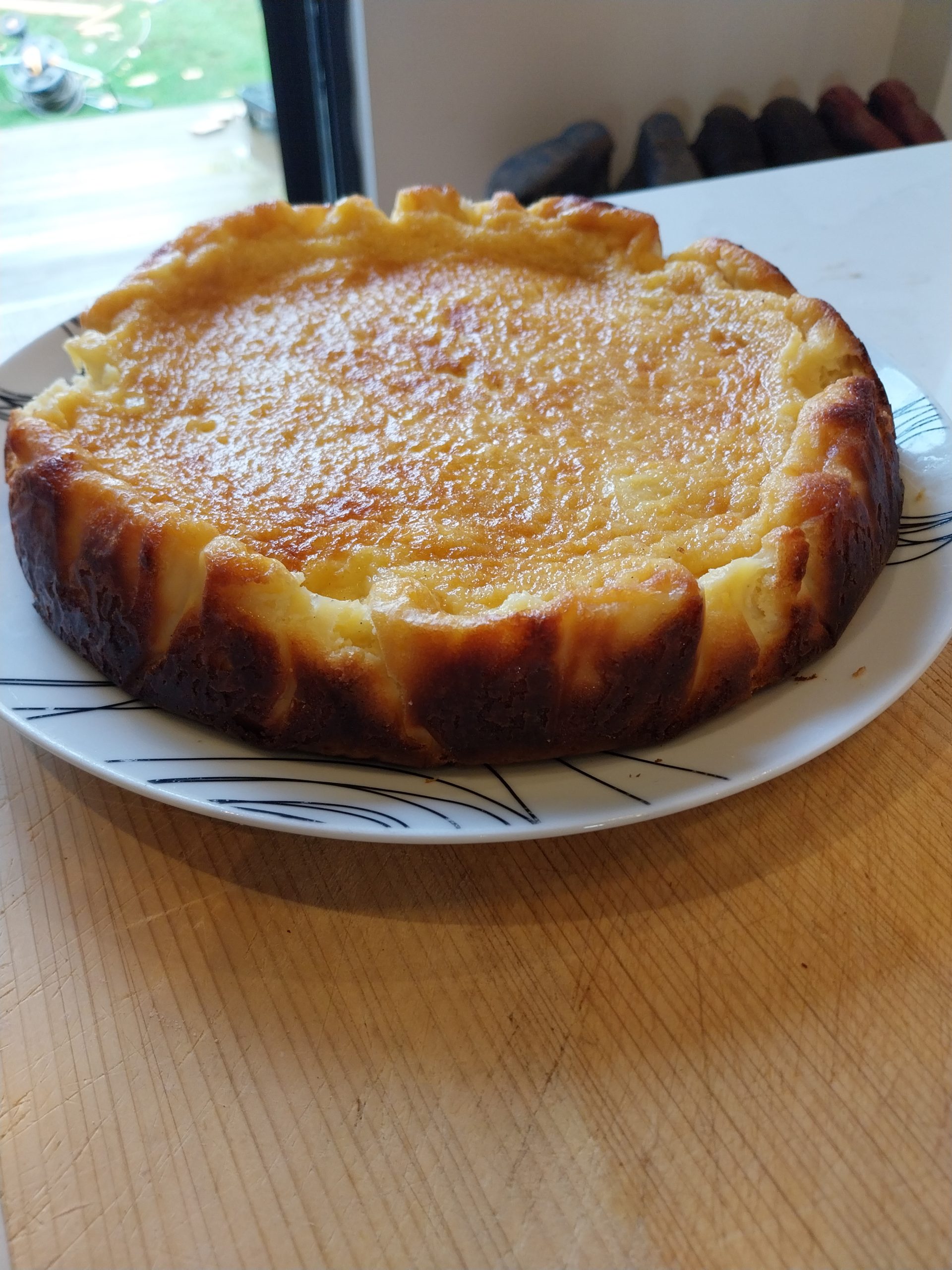 The cheesecake out of the tin on a white plate, golden on top with dark sides
