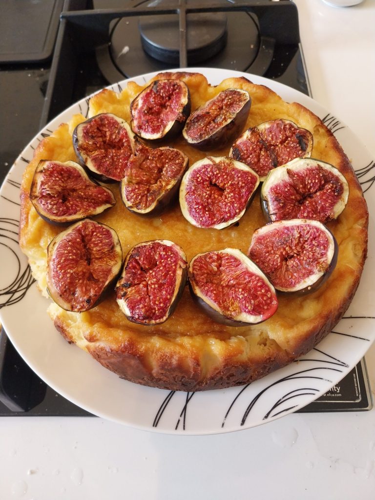 A Basque cheesecake on a white plate topped with twelve grilled fig halves, cut side up