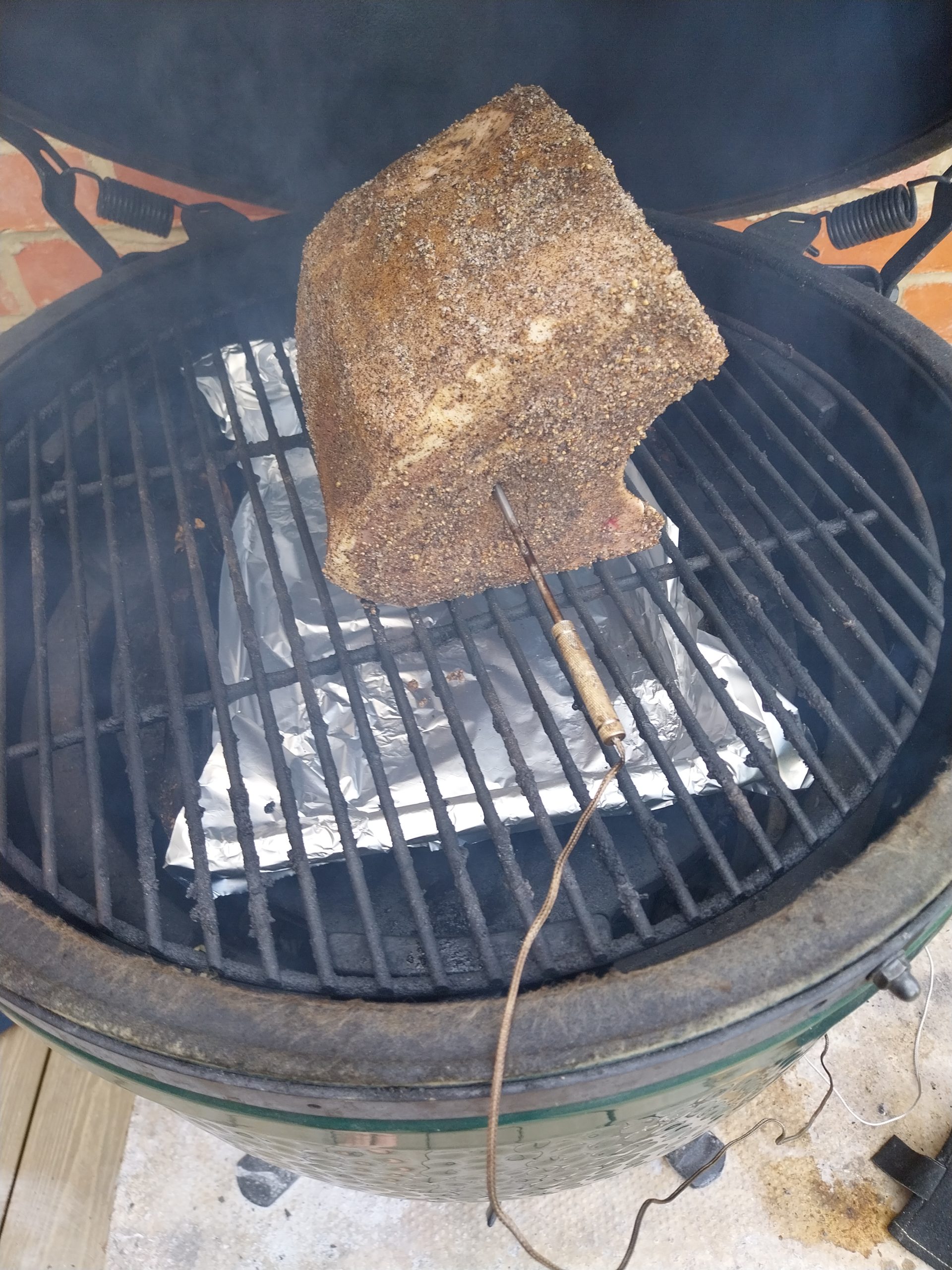 The rubbed pork loin on the grate of a Big Green Egg with a probe in it and a foil drip tray below