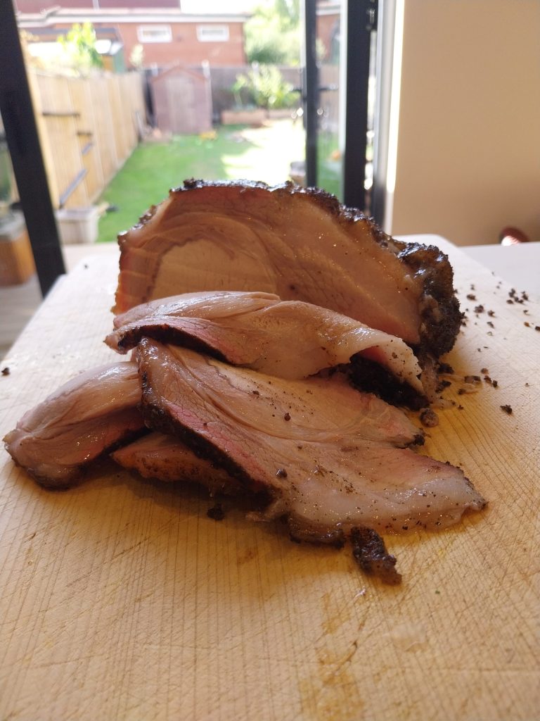 A pork loin with the bones off, sliced on a wooden board, pink under a dark peppery crust