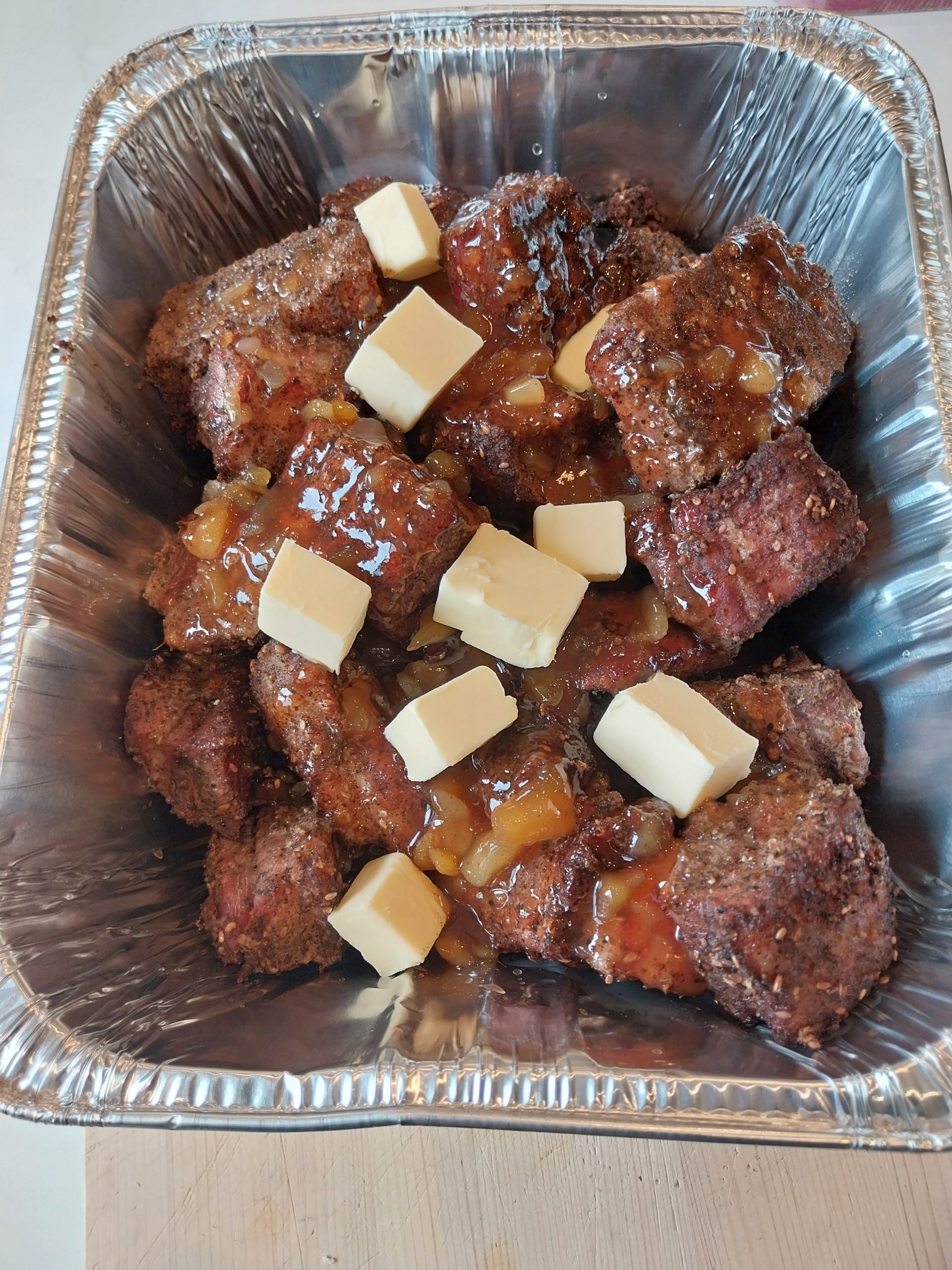 The pork belly chunks in a foil tray with mango chutney and cubes of butter on top