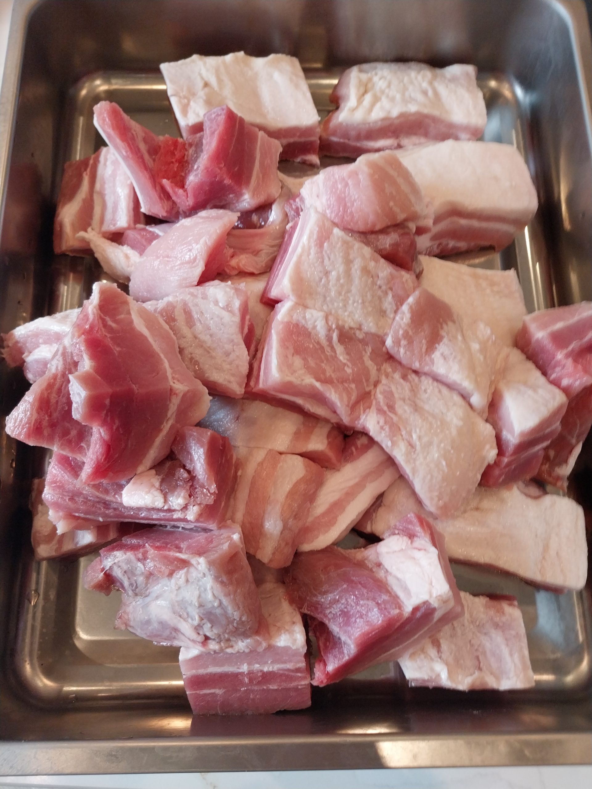 Pork belly cut into big chunks in a steel tray, skin off