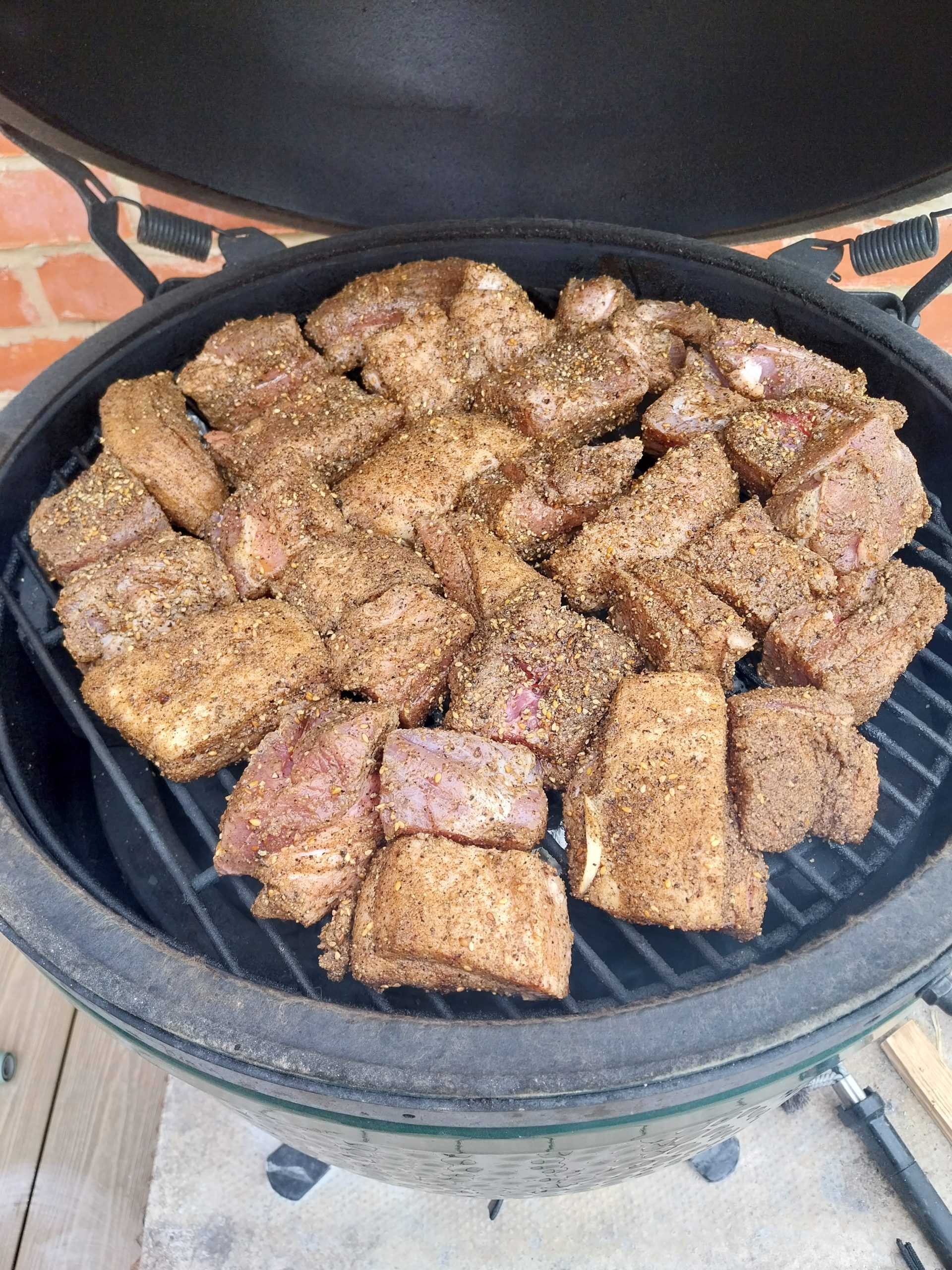 Rubbed pork belly chunks in a single layer on the grate of a Big Green Egg, lid open