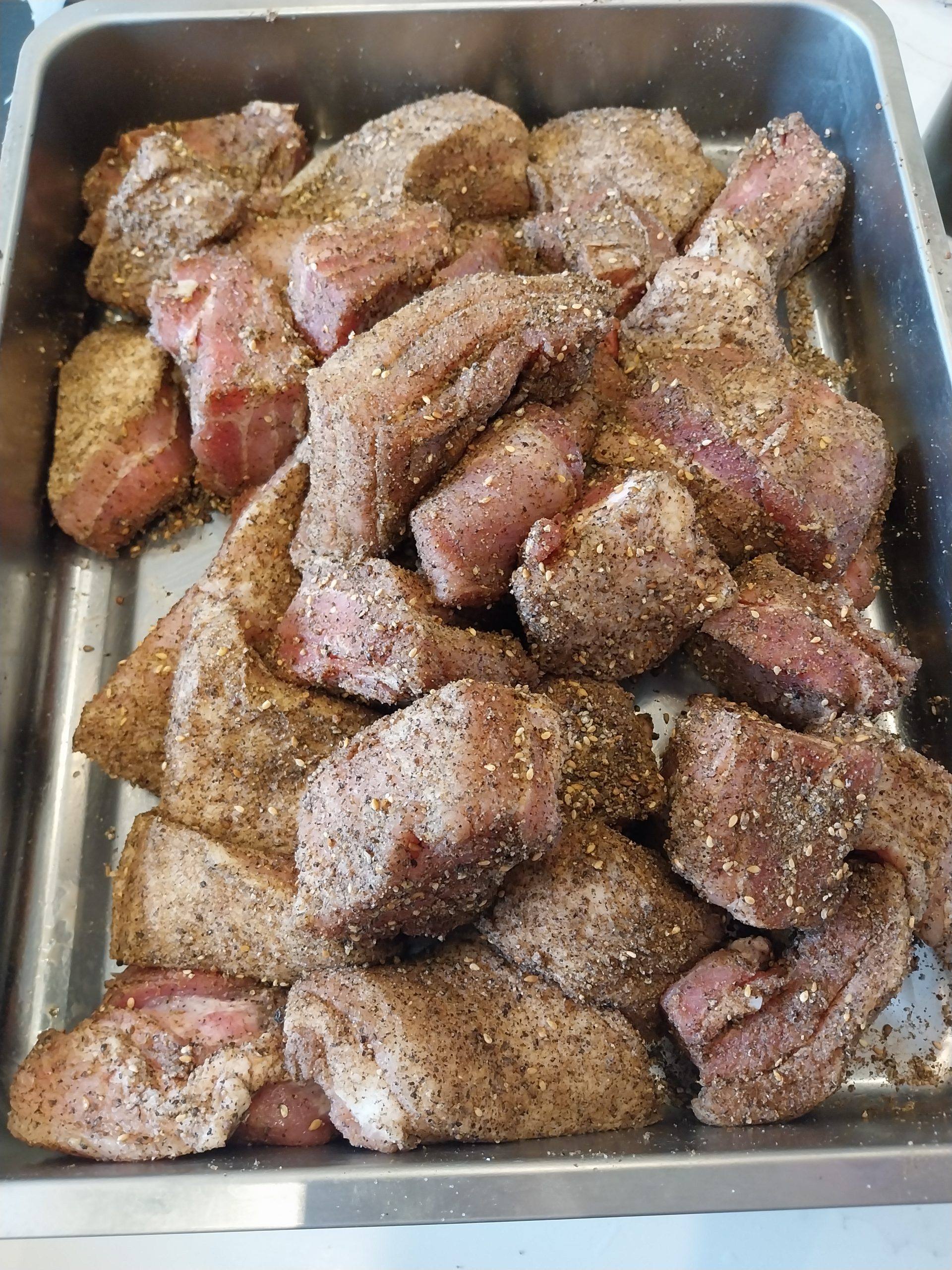 The pork belly chunks in a steel tray, coated in a pepper and Ras el Hanout rub