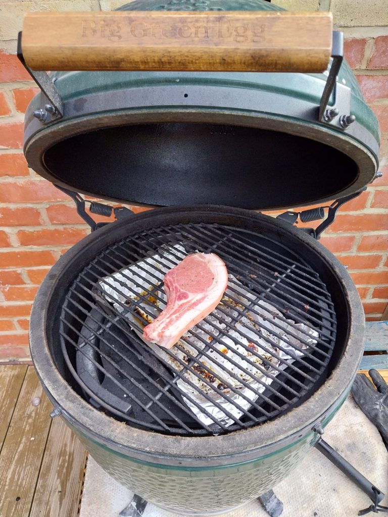 The pork chop on the Big Green Egg grate, set up indirect with the deflector and a foil drip tray underneath