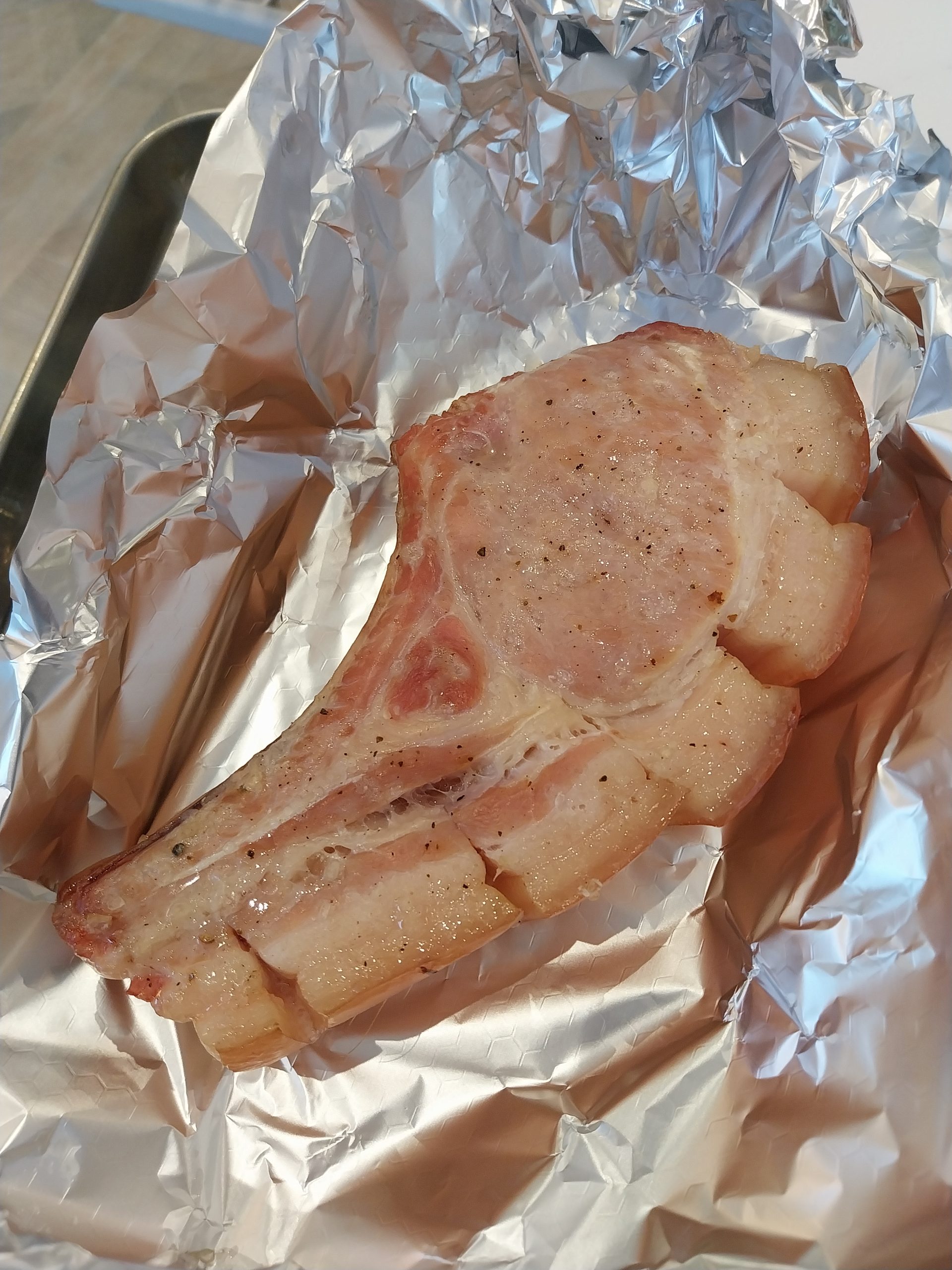The pork chop resting on foil after the indirect cook, before the sear