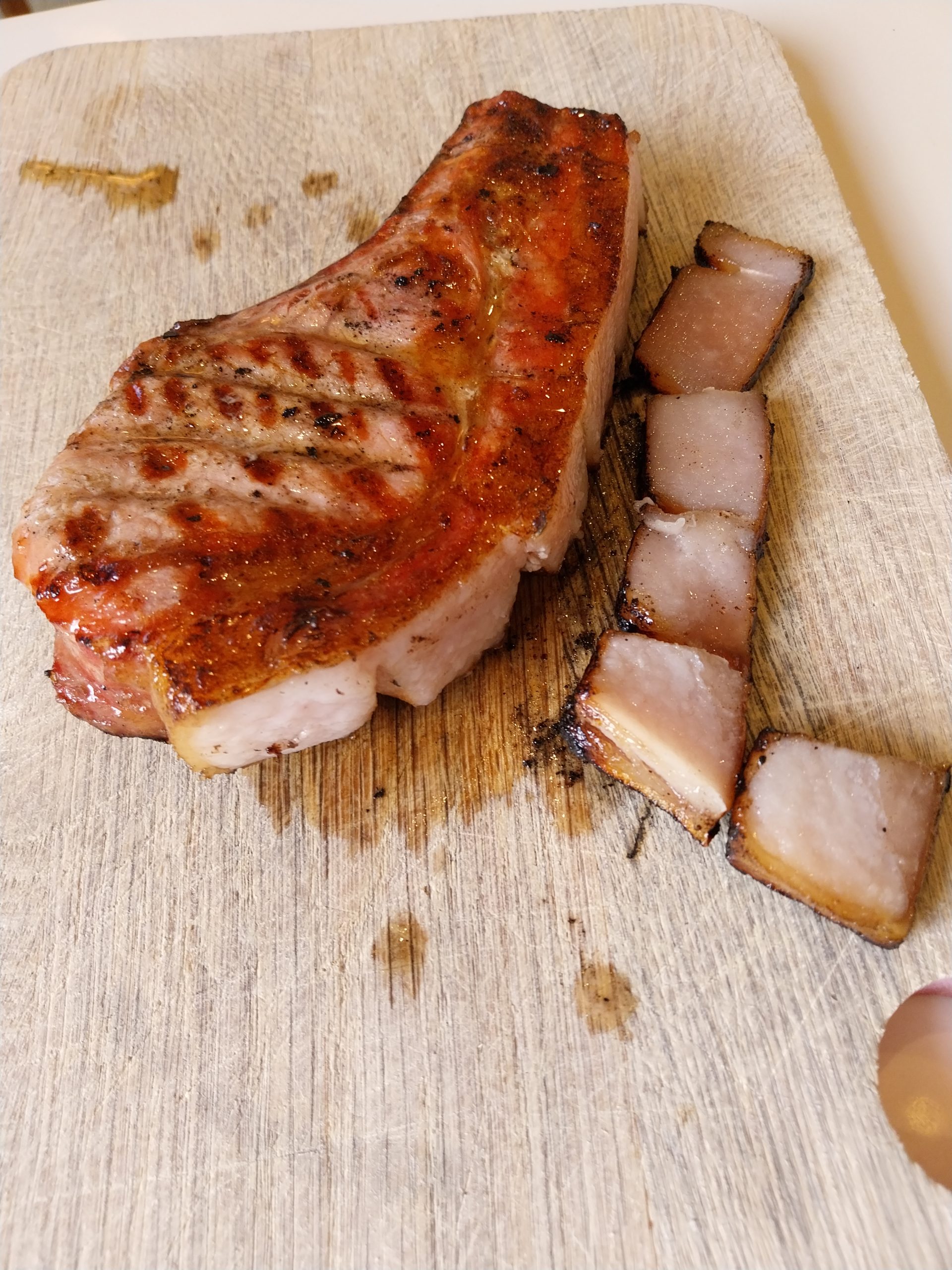 The seared pork chop on a board with the rind cut off beside it